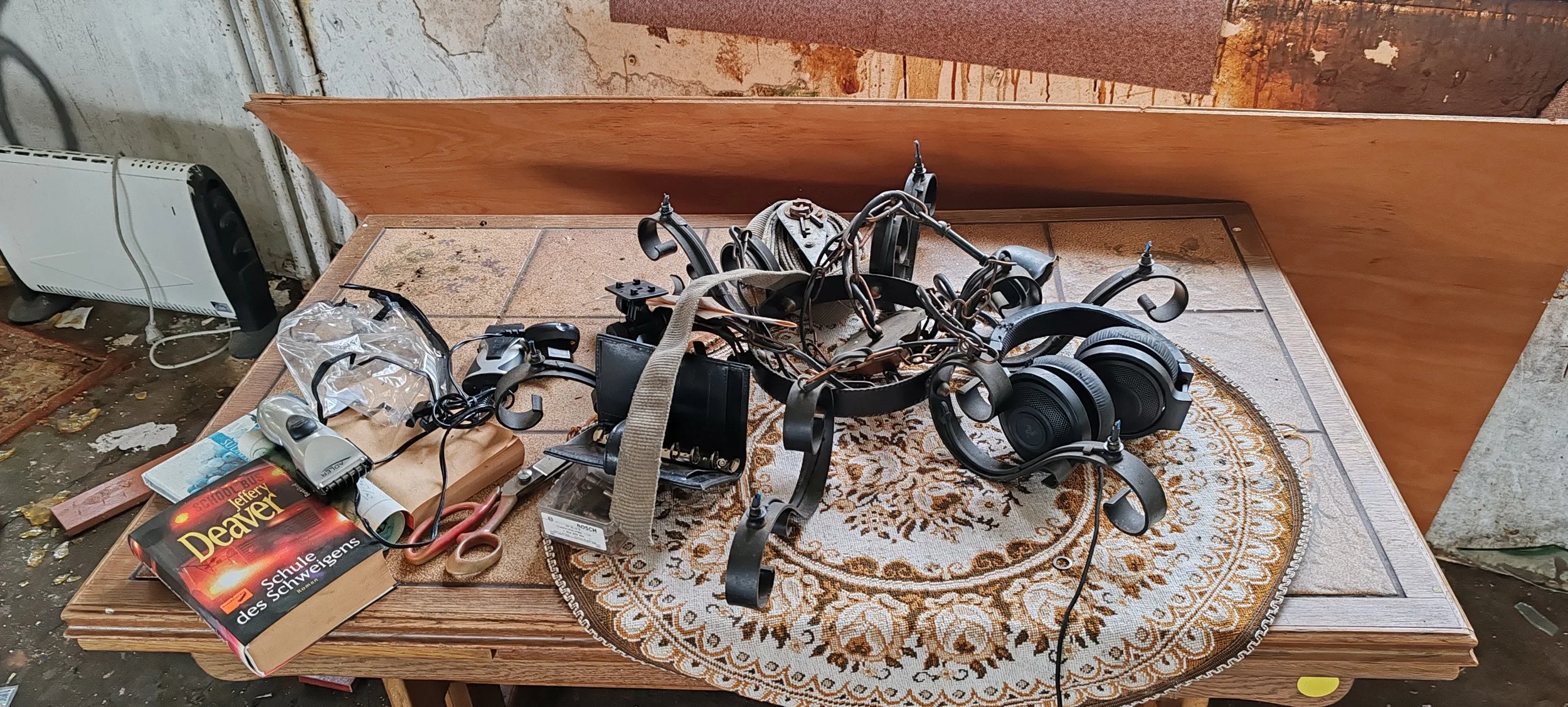 Veraltete elektronische Geräte, Kopfhörer, Kabel und eine Schulbuch auf einem Tisch mit einem kleinen Teppich. Im Hintergrund eine Heizung und eine Wand.