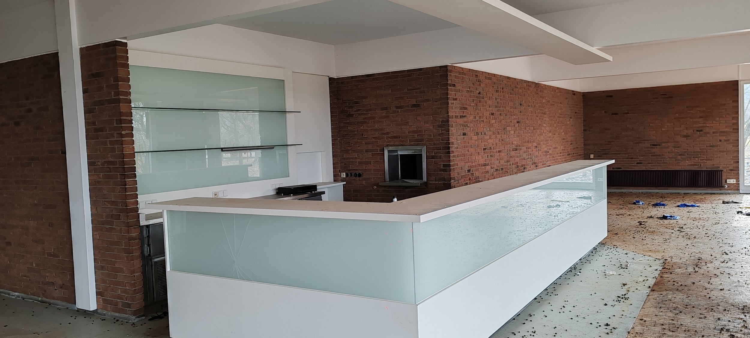 Modern offene Küche mit einer weißen Bar, Backsteinmauer, Kamin, schmutzigem Boden und unordentlichem Raum.