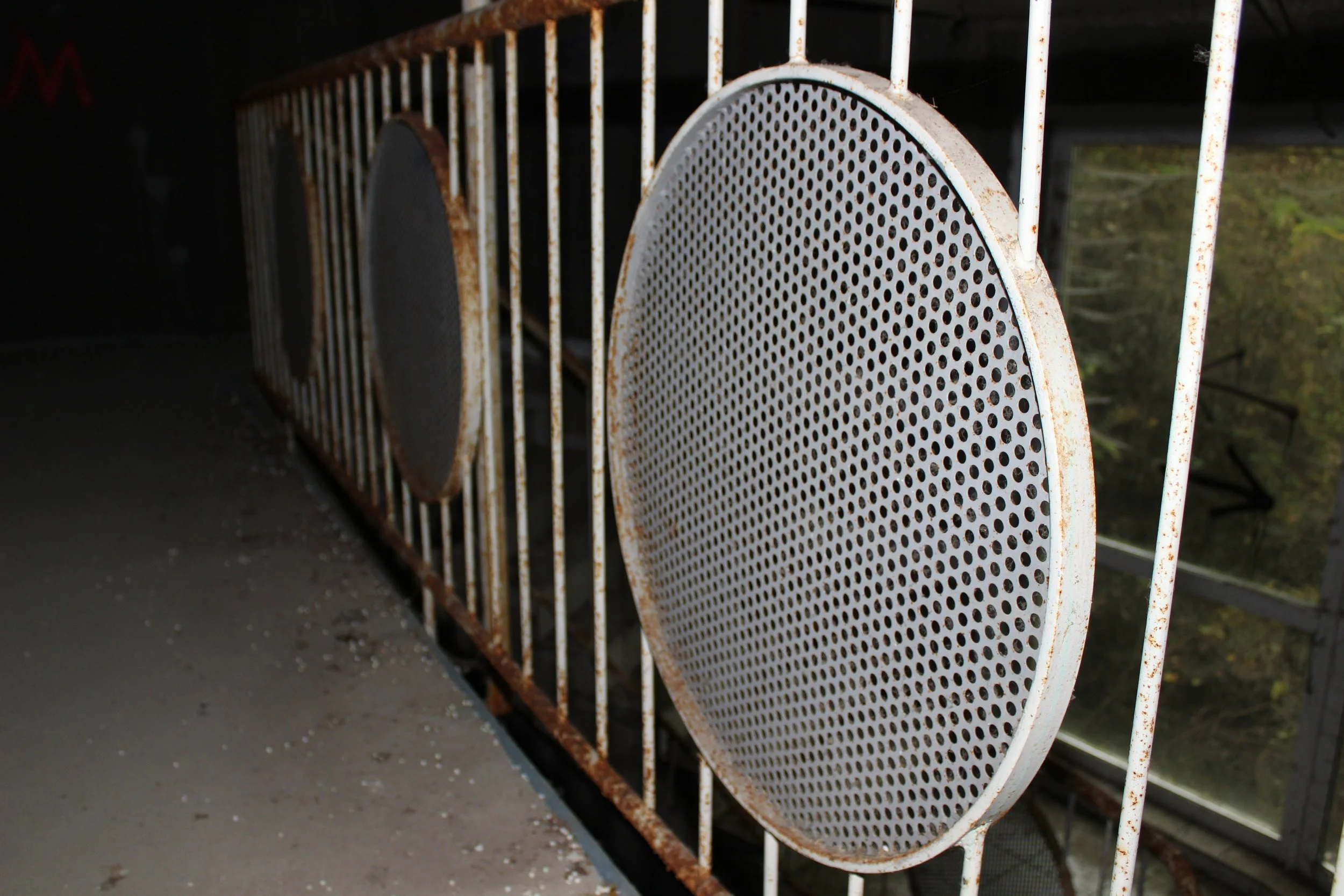 Alte, rostige Metallkonstruktion mit runden Gitterplatten in einer dunklen, verfallenen Umgebung.