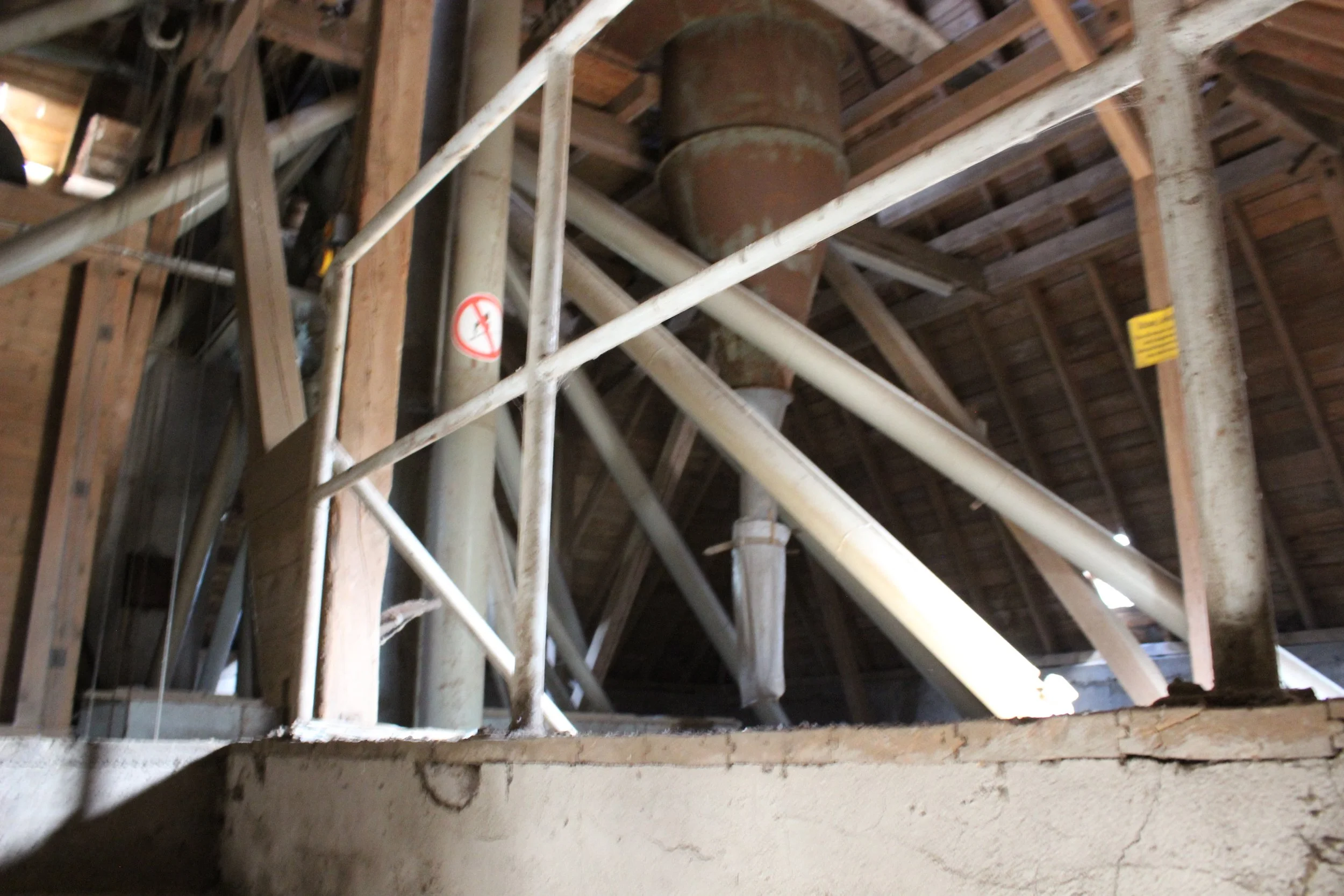 Innenansicht eines Dachbodens mit Holzbalken, Dachziegeln und einer Lüftungsanlage, mit Schutzgeländer und warnhinweis