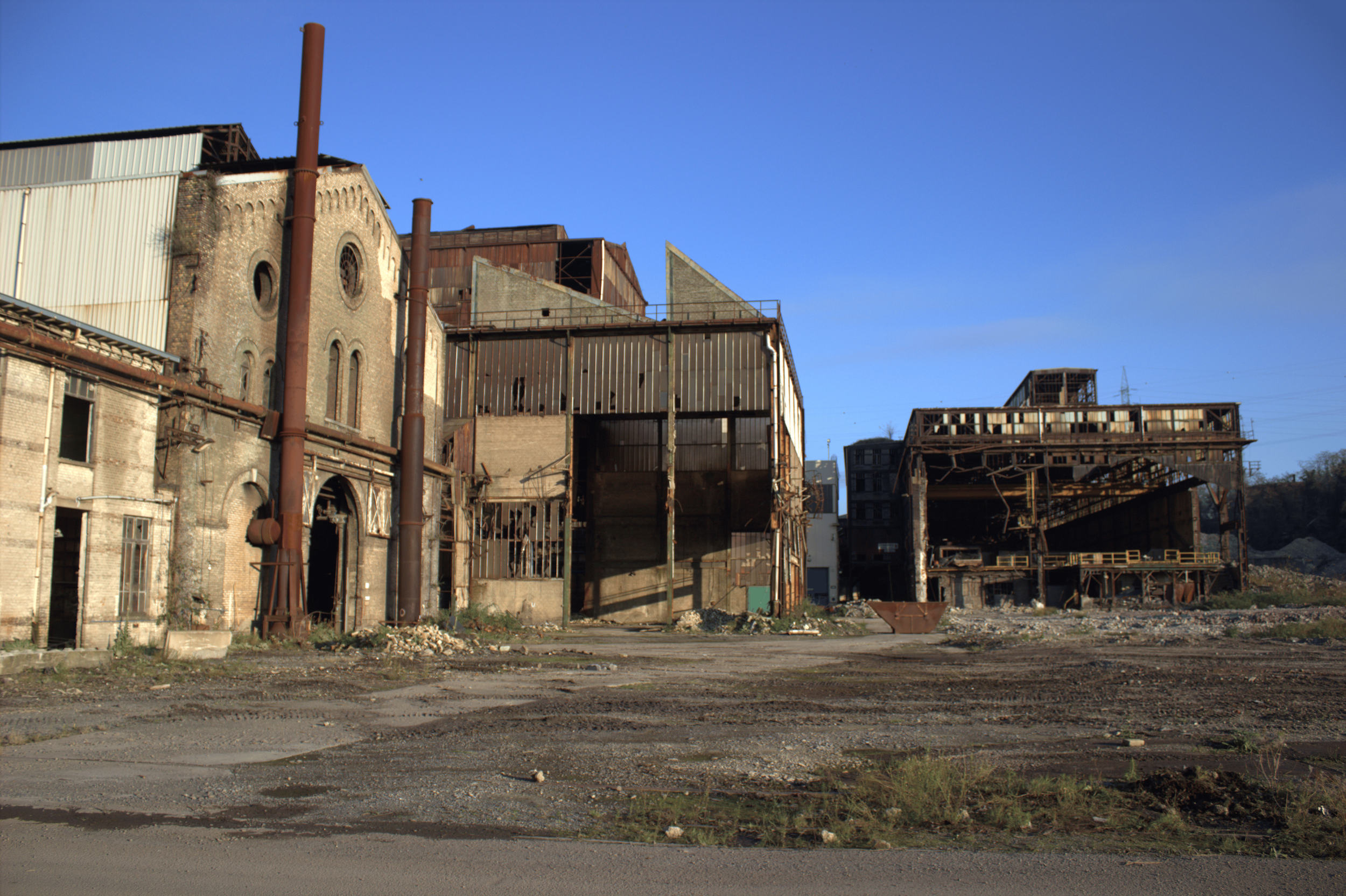 Verfallene Industriegebäude mit rostigen Rohren und zerfallender Struktur unter blauem Himmel.