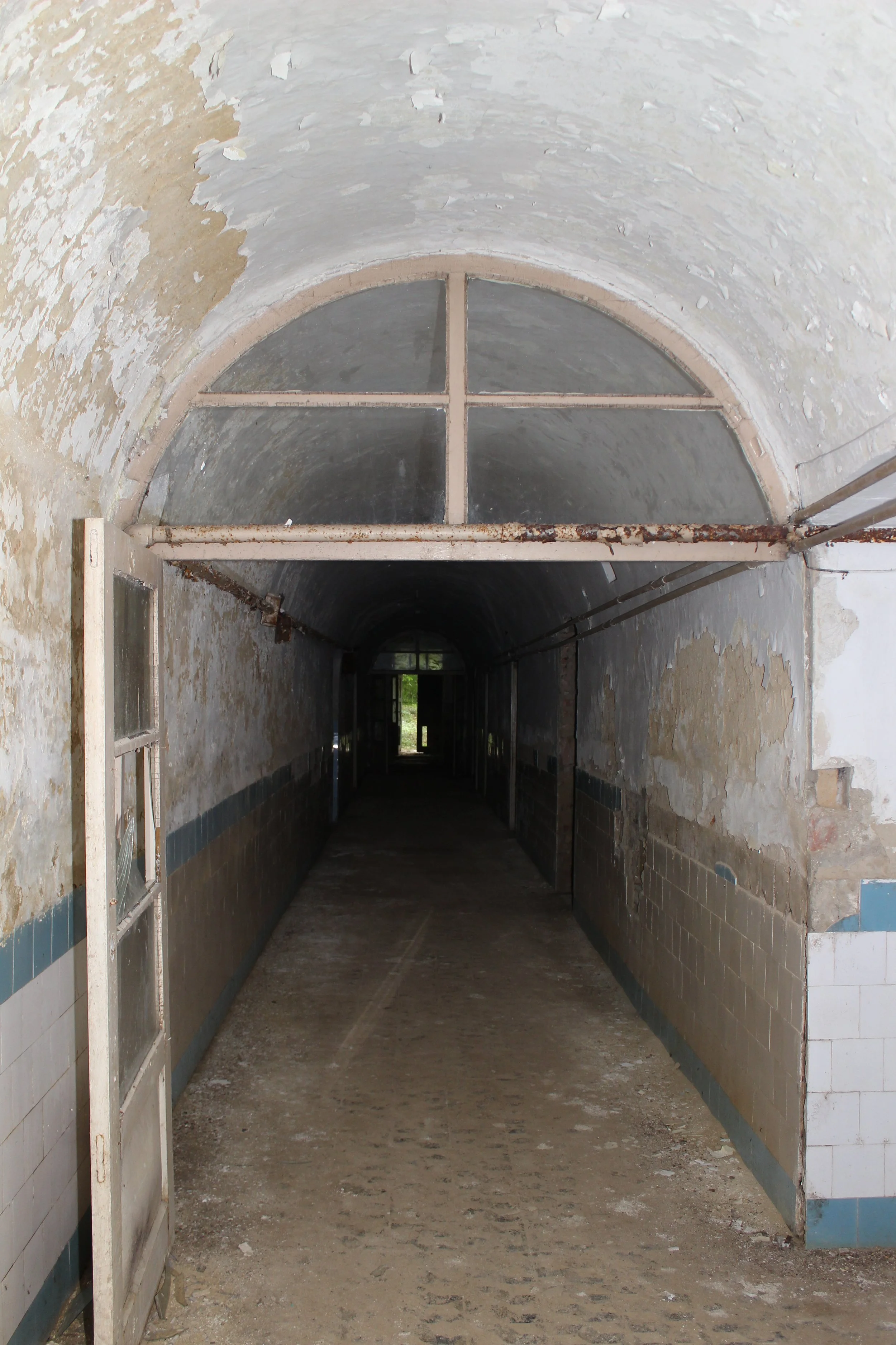 Ein verlassener, alter Korridor mit abblätternder Wandfarbe und einer halb offenen Tür am Anfang, Blick in die Dunkelheit.