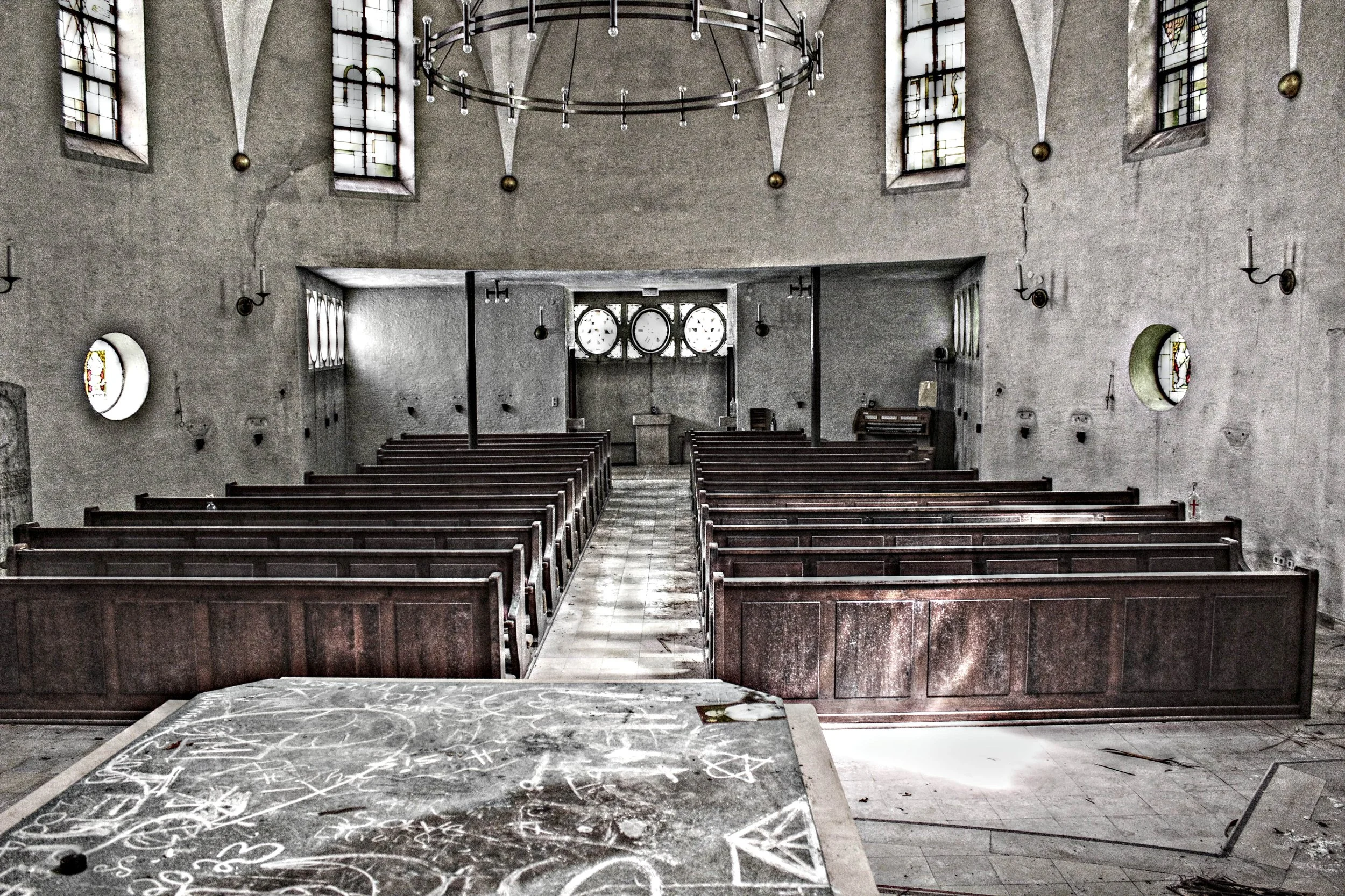Verlassene Kirche mit leeren Bänken, einem schwarzen Brett, einer Mischung aus Kerzenhaltern an den Wänden und bunten Glasfenstern, die das Licht hereinlassen, von oben sichtbar.