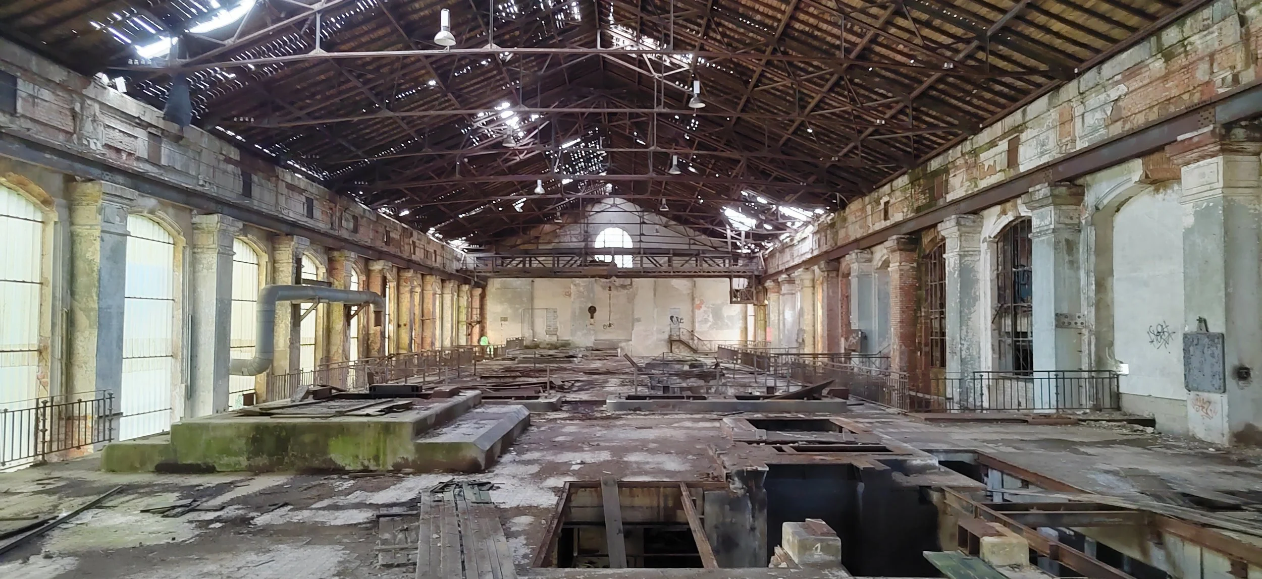 Großes verfallenes, vernachlässigtes Gebäude mit hohem Dach und Fenstern an den Seiten, zerbrochenen Böden und sichtbarer Infrastruktur, Relikte vergangener Nutzung.