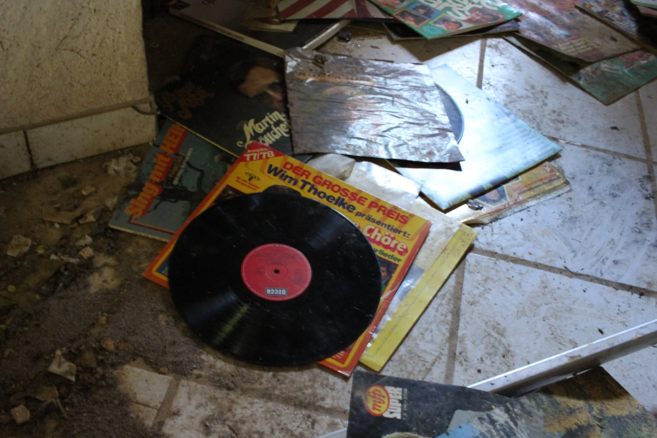 Alte verstreute Platten und Vinylschallplatten auf einem Boden, darunter ein Vinyl mit rotem Etikett.