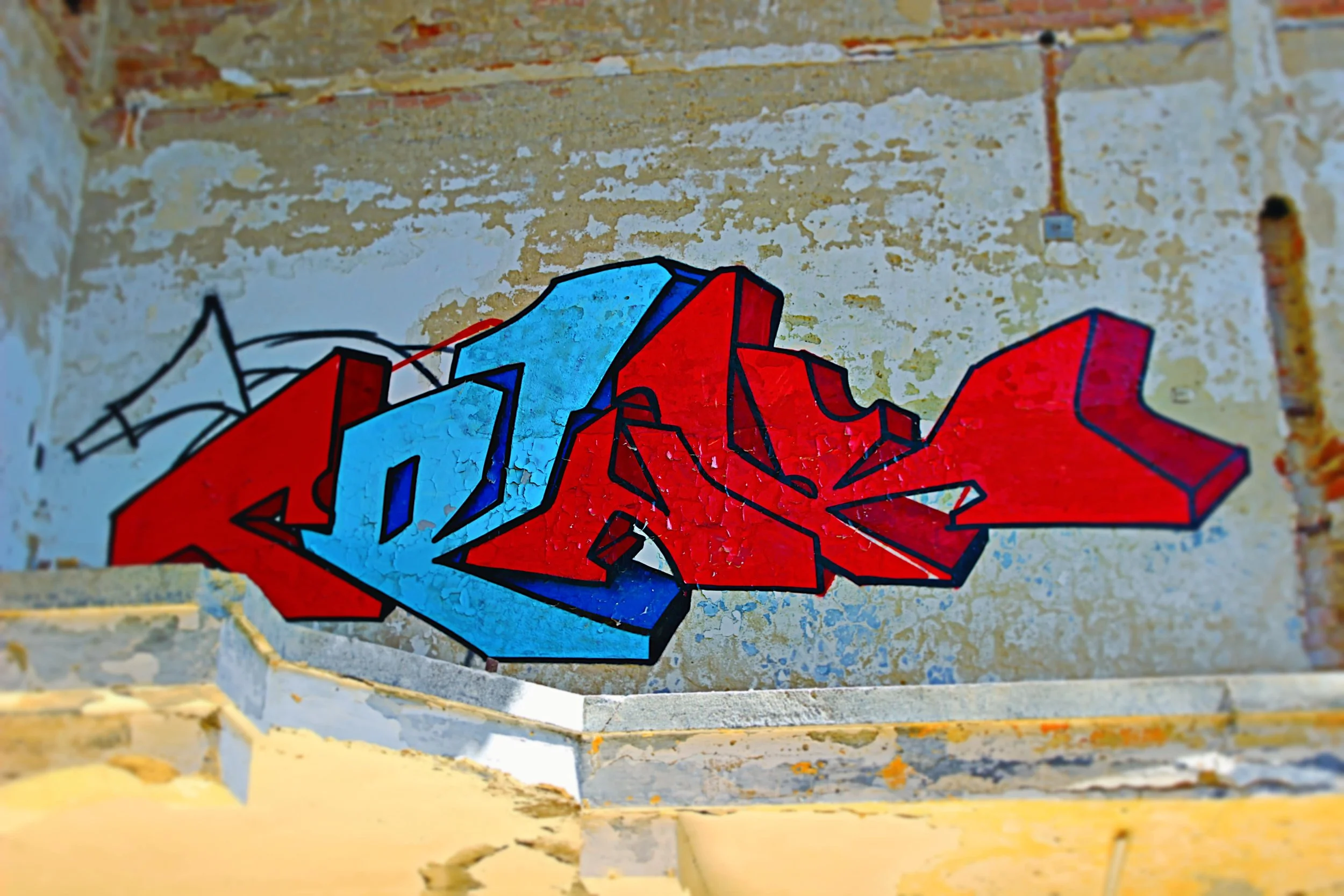 Graffiti mit roten, blauen und schwarzen Konturen auf einer alten, beschädigten Wand.