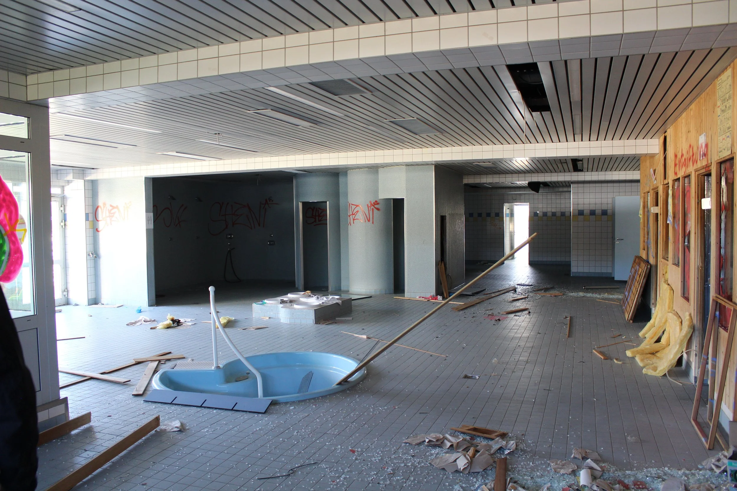 Innenraum eines zerstörten Gebäudes mit zerbrochenem Boden, herumliegendem Schutt, einem zerstörten Whirlpool, zerstörten Wänden und Graffiti auf den Wänden.