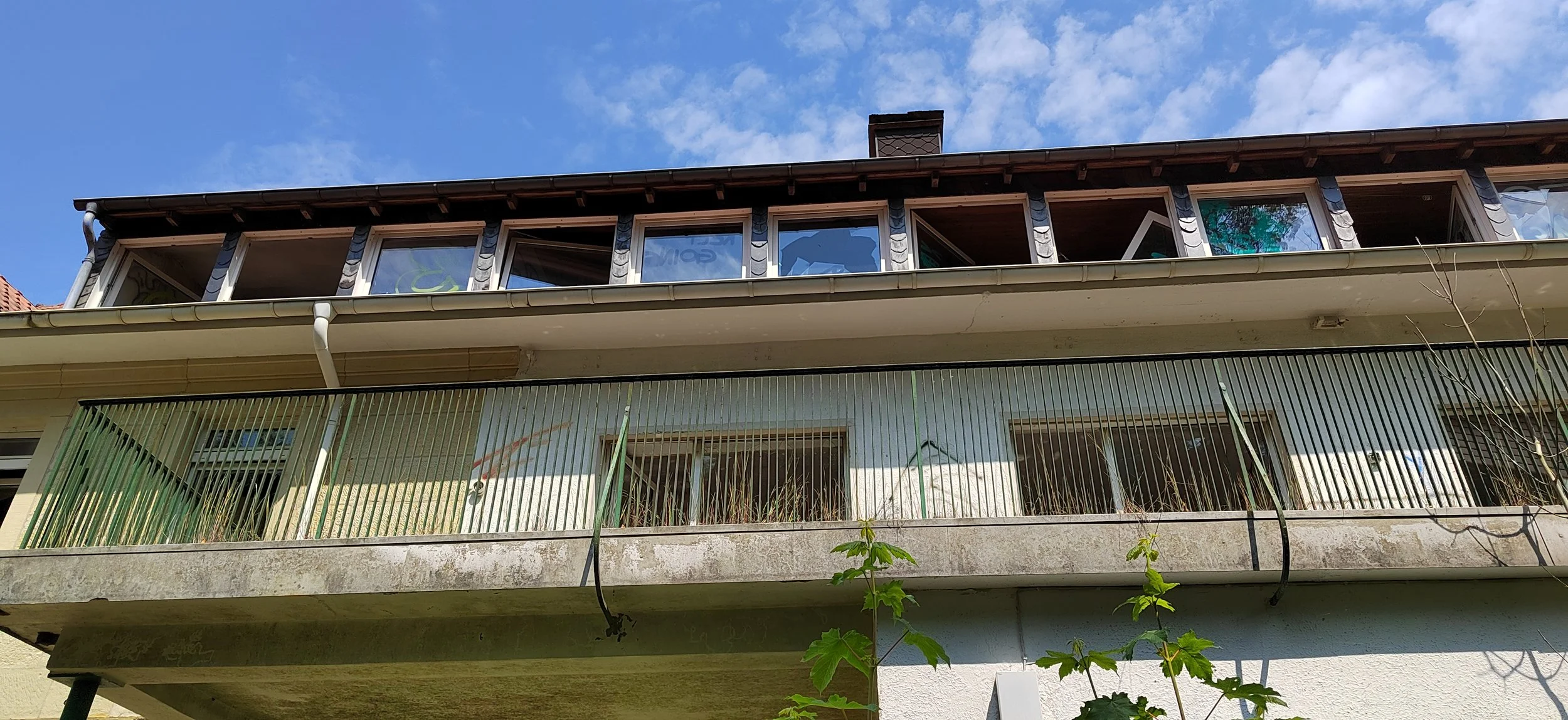 Mehrstöckiges Wohngebäude mit Fenster und Balkon, Baum im Vordergrund, blauer Himmel mit Wolken.