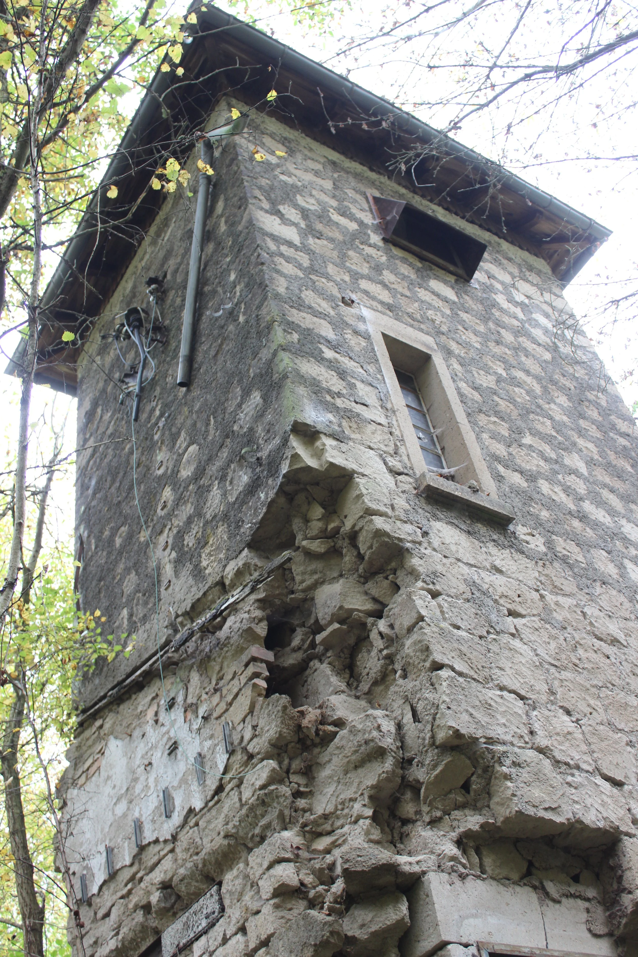 Ein verfallenes, altes Steinhaus im Wald mit beschädigter Fassade, zerbrochenen Steinen und offenem Fenster.