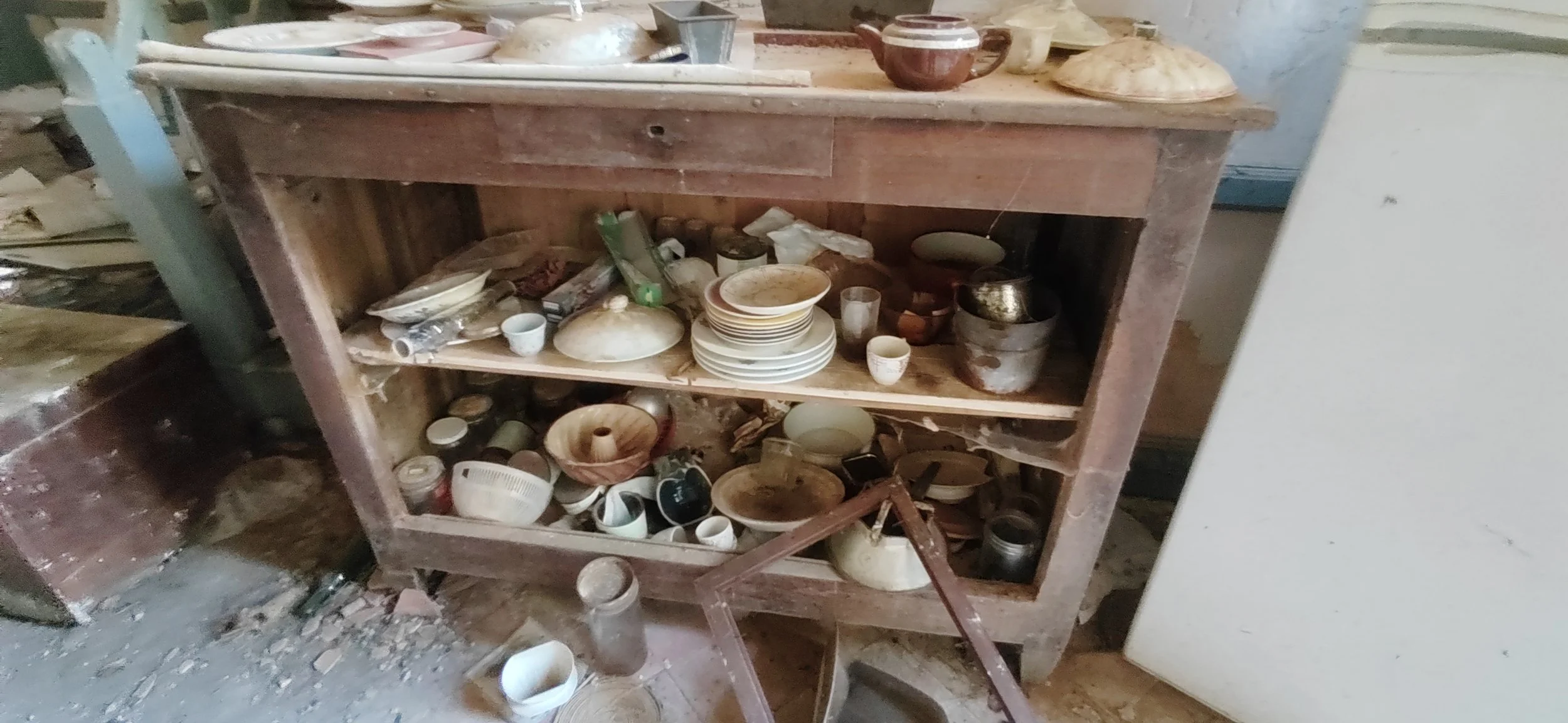 Verstaubter Holzbücherschrank mit schmutzigem Geschirr und Krümeln, Chaos im Raum.