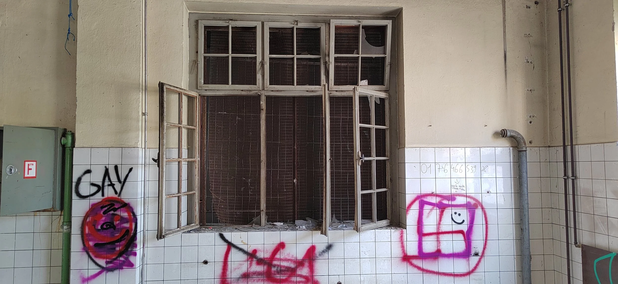 Verwahrloste, alte Fenster in einer grauen Wand, Graffiti und Leuchtreklame auf den Fliesen, Schmutz und Dreck im Raum.