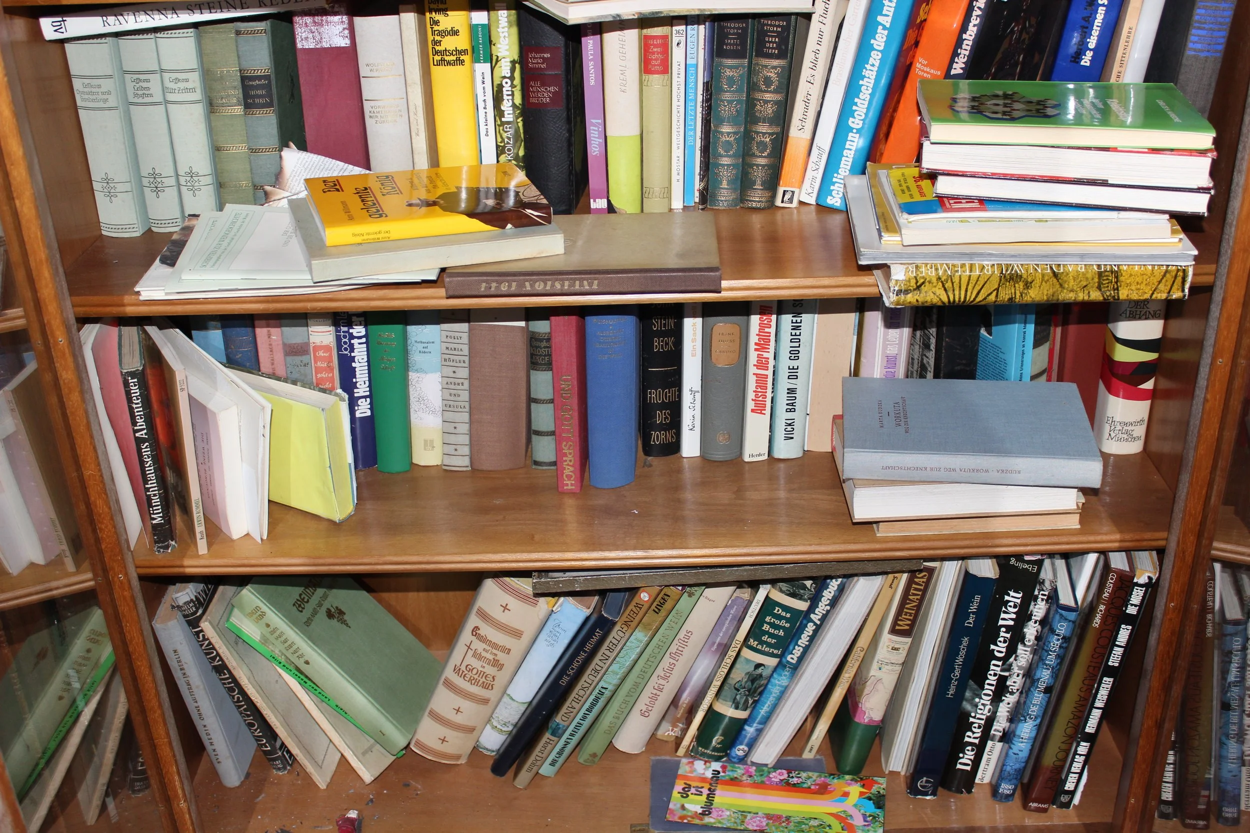 Buchregal mit mehreren Regalen voller Bücher in verschiedenen Farben und Größen, einige Bücher liegen flach auf den Regalen, und es ist eine bunte Karte am Boden sichtbar.