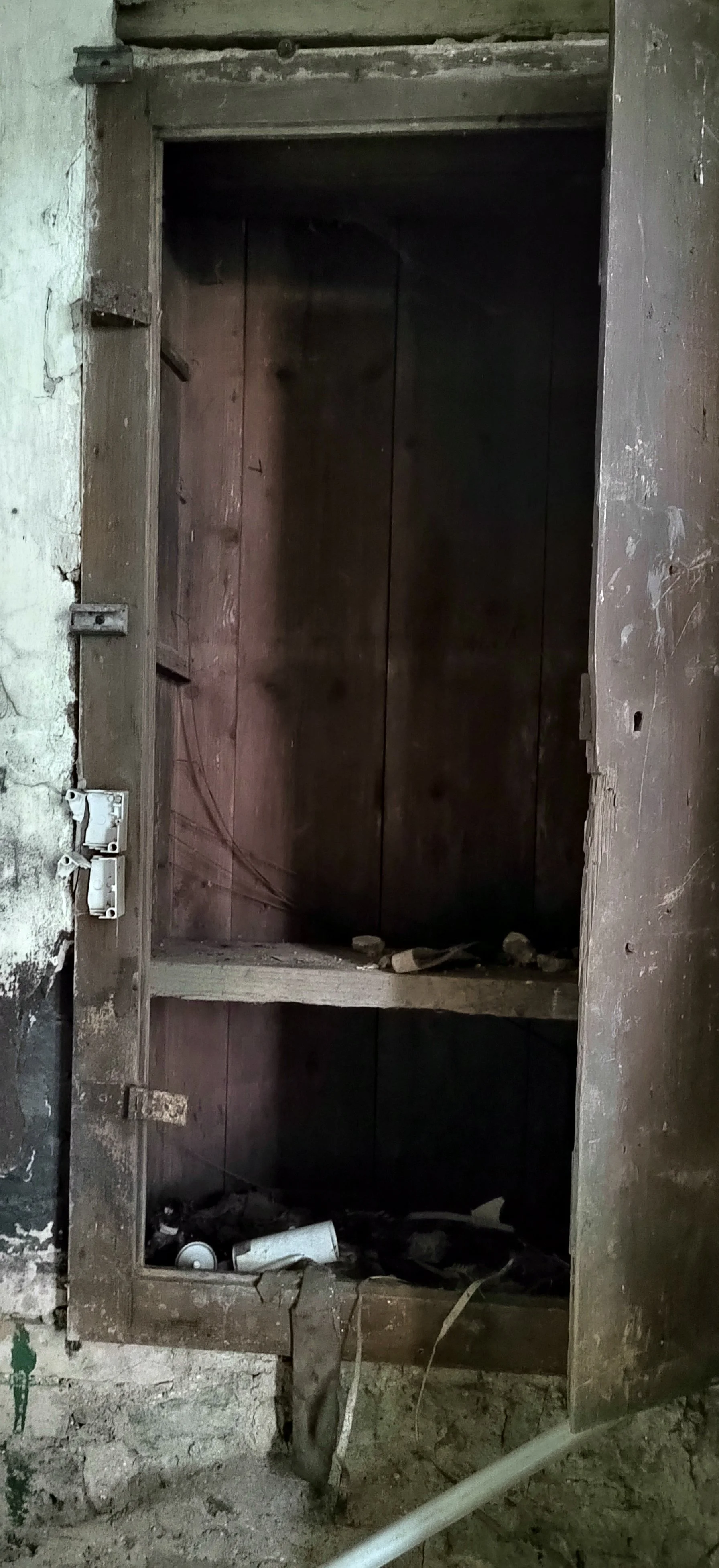 Ein alter, leerer Holzkasten oder Schrank mit einem verfallenen und schmutzigen Inneren, teilweise mit Müll und Staub bedeckt.