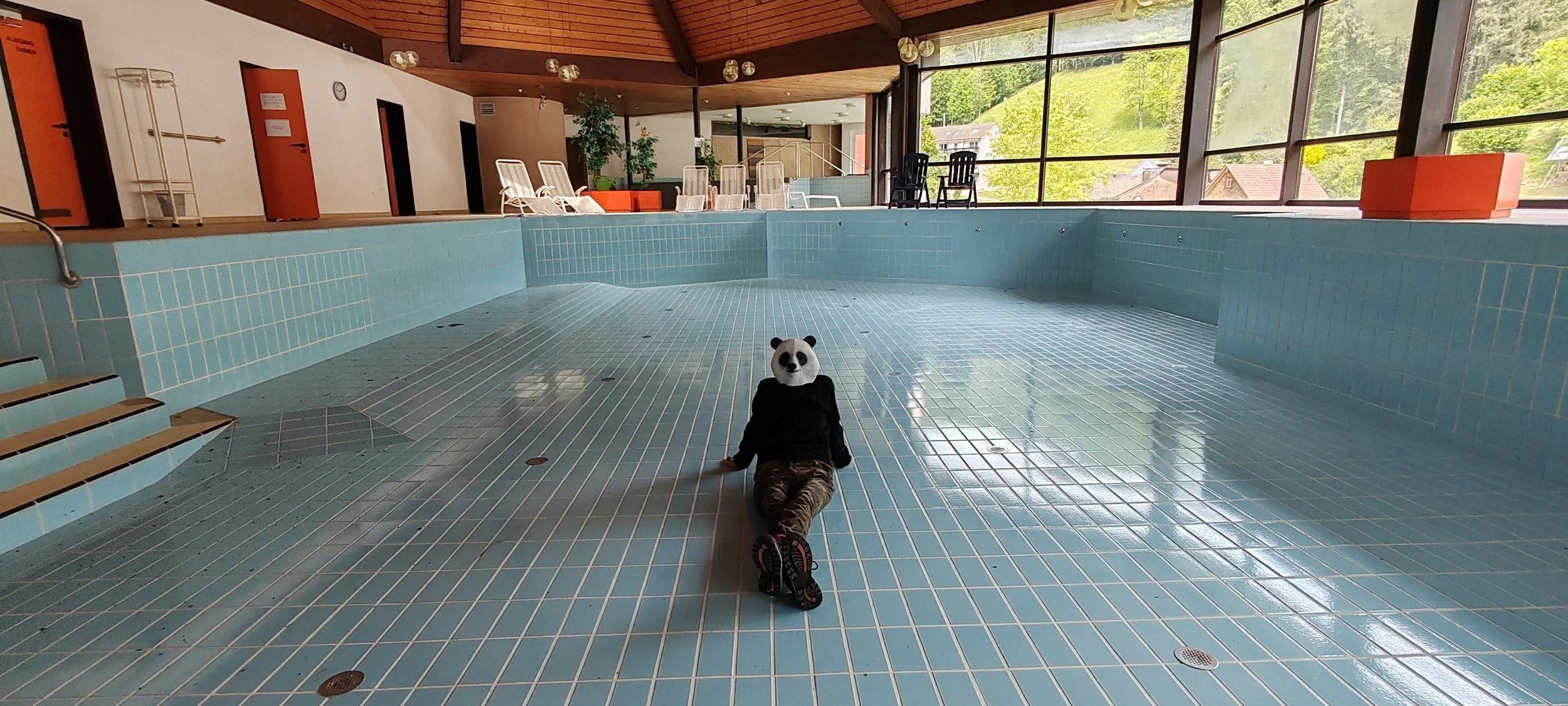 Innenraum eines leeren Schwimmbads mit person mit Panda-Maske, die auf dem Boden liegt.