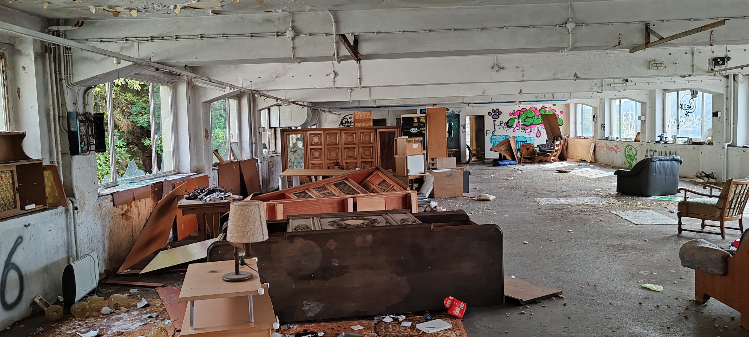 Ein verlassener Raum mit zerstörtem Mobiliar, zerbrochenen Fensterscheiben und Graffiti an den Wänden, voller Unordnung und Staub.
