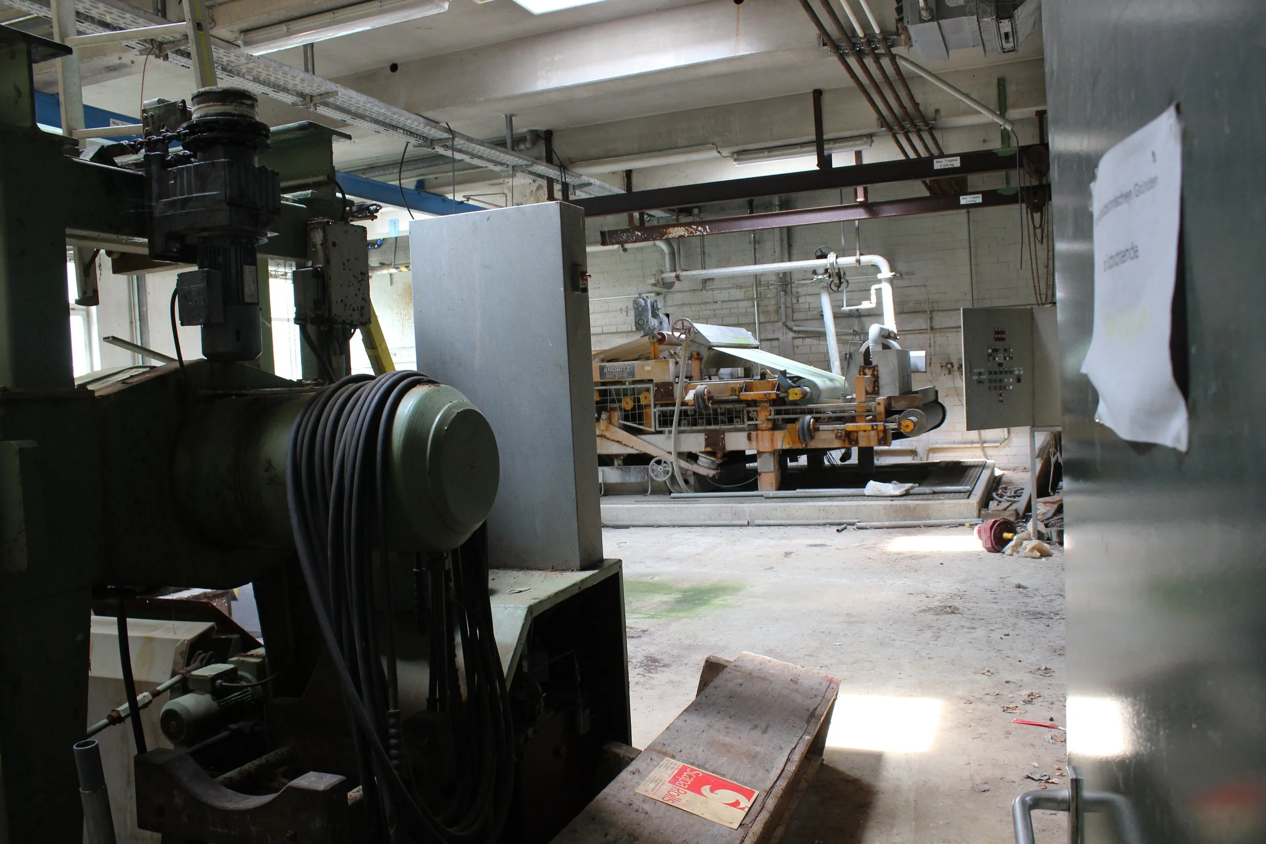 Ein Industrieraum mit Maschinen, Leitungen und einer Ablagefläche, der Arbeitsbereich ist unordentlich und teilweise beschädigt.