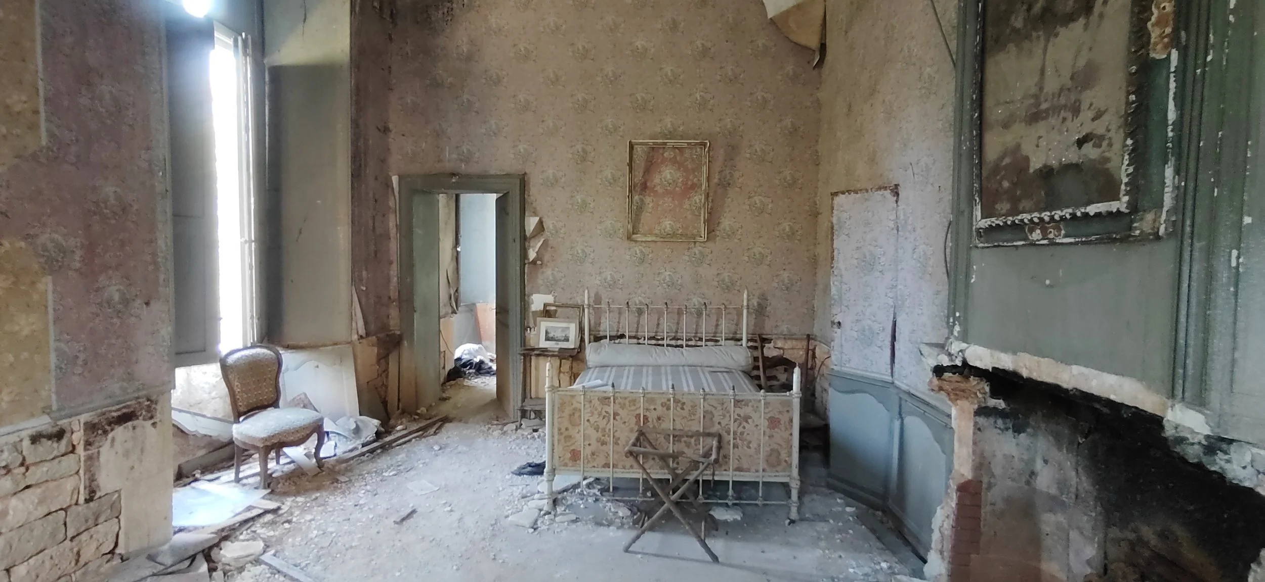 Verlassene ruinöse Schlafzimmer mit antikem Bett, zerbrochener Wand und alten Möbeln.