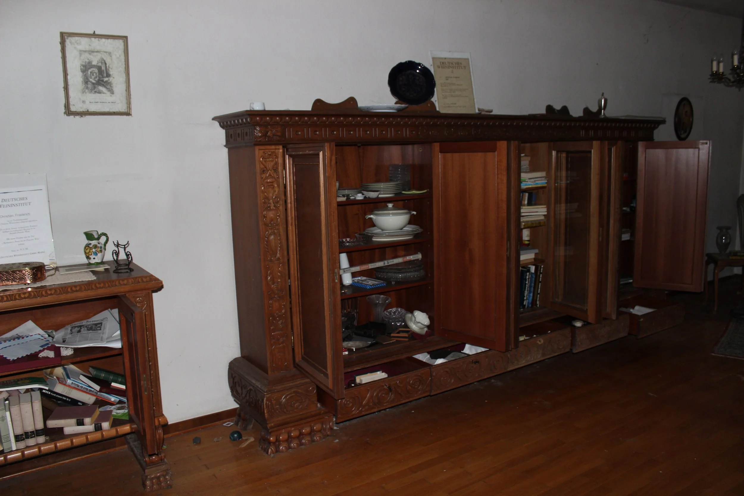 Ein Holzkabinett mit aufgeschlagenen Türen, gefüllt mit Geschirr und Büchern, in einem Raum mit Holzboden