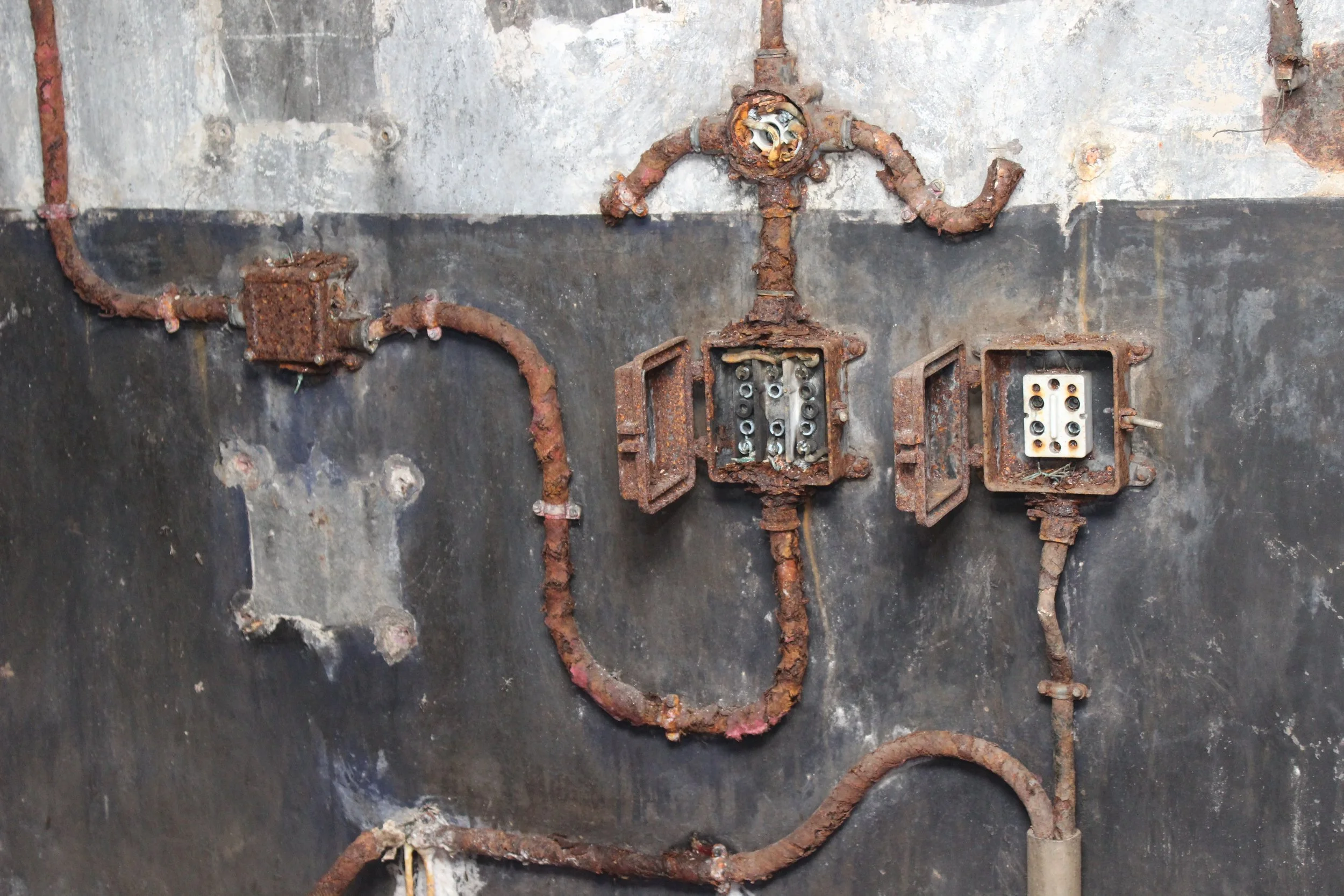 Alt: Rostige alte elektrische Verkabelung auf einer Wand, die Kabel sind teilweise beschädigt oder fehlen. Es ist ein veraltetes und beschädigtes Elektriksystem sichtbar.