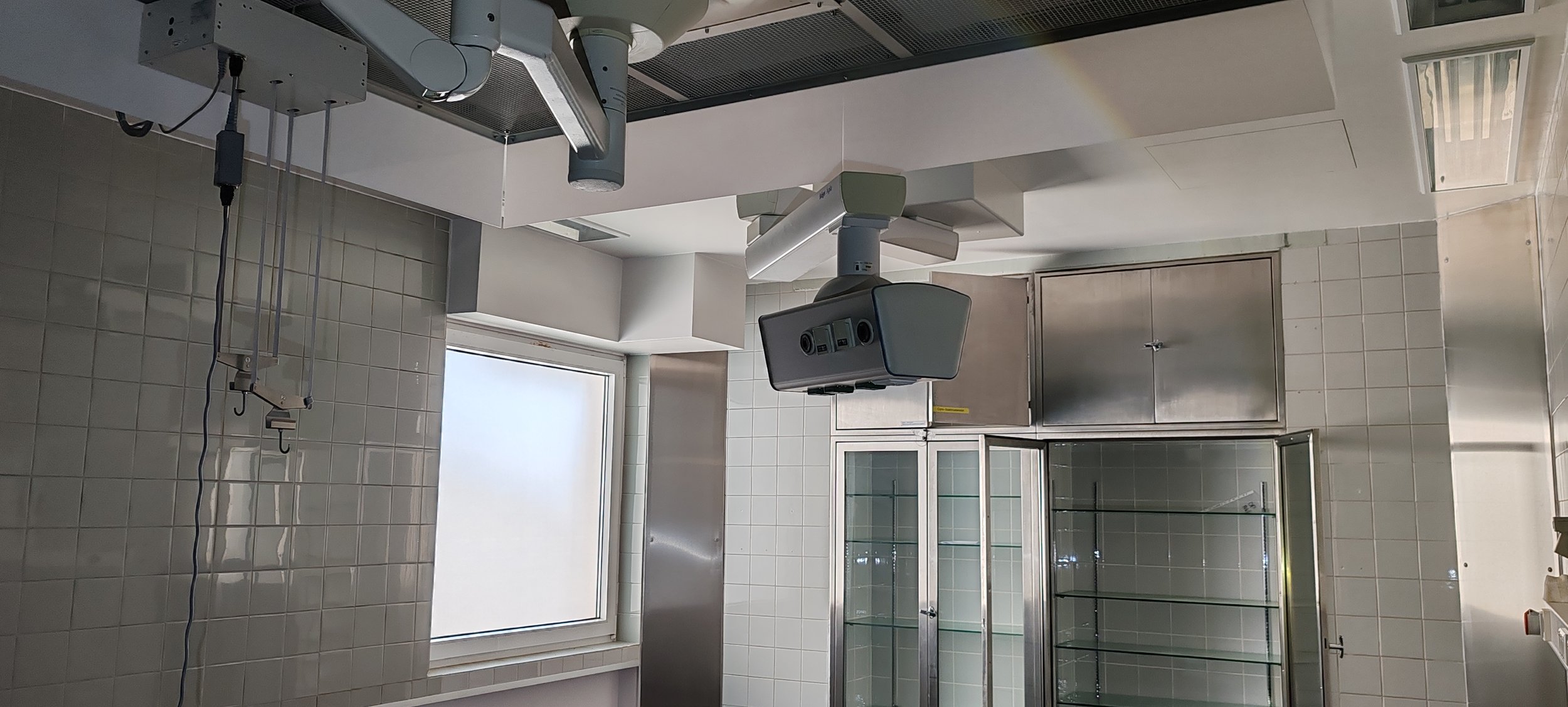 Ein Operationssaal mit medizinischer Ausrüstung, darunter ein computergesteuertes chirurgisches Robotersystem, in einem hell erleuchteten Raum mit weißen Fliesen und einem Fenster.