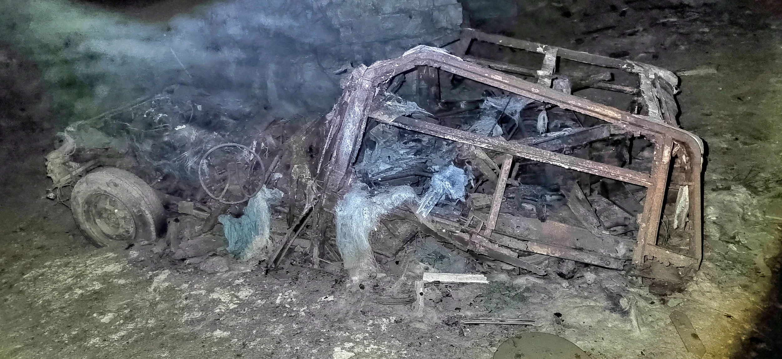 Verbrannter, zerstörter Autowrack auf dem Boden, Rauch und Trümmer rundherum.