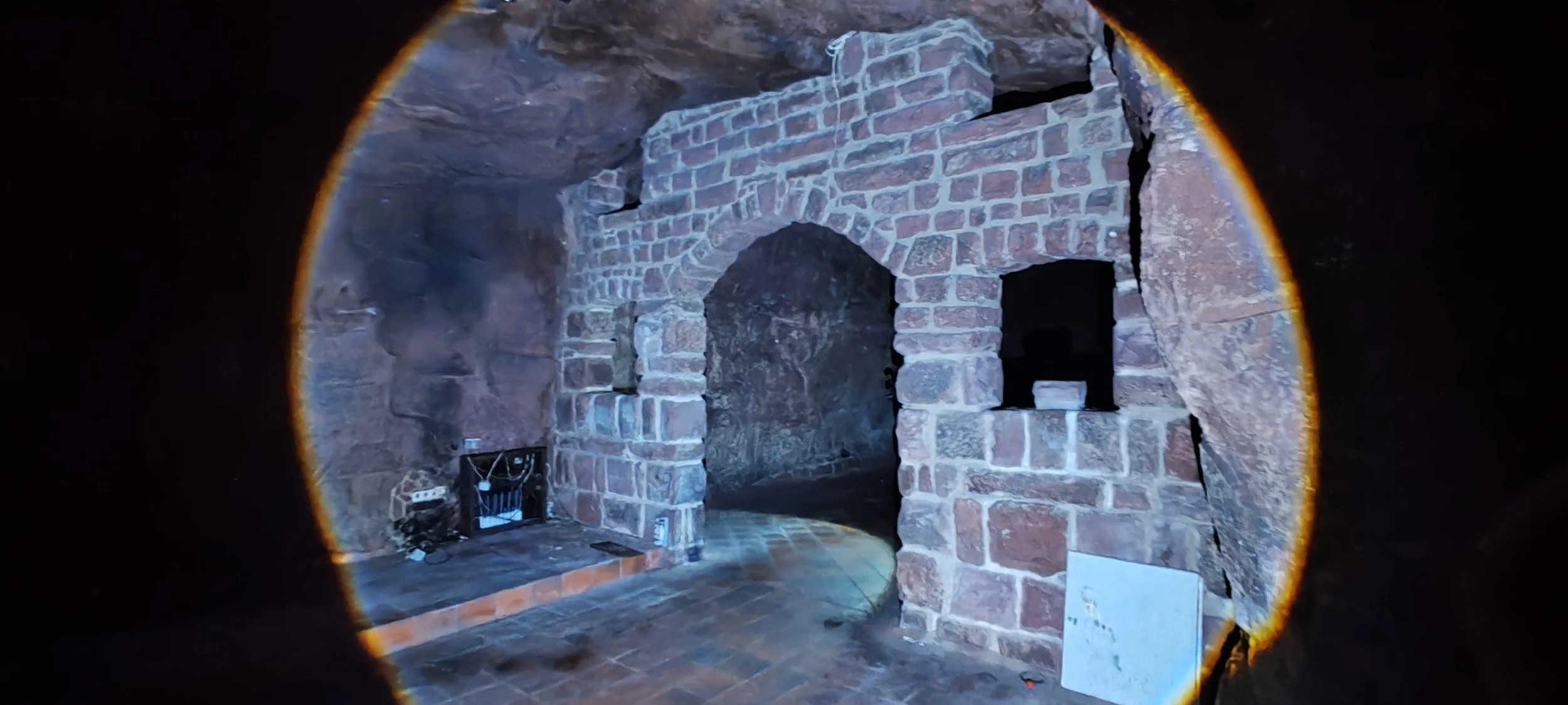 Innenansicht eines alten Gemäuers mit Backsteinmauern und einem Rundbogentor. Es gibt eine elektrische Verkabelung und einige Steine auf dem Boden.