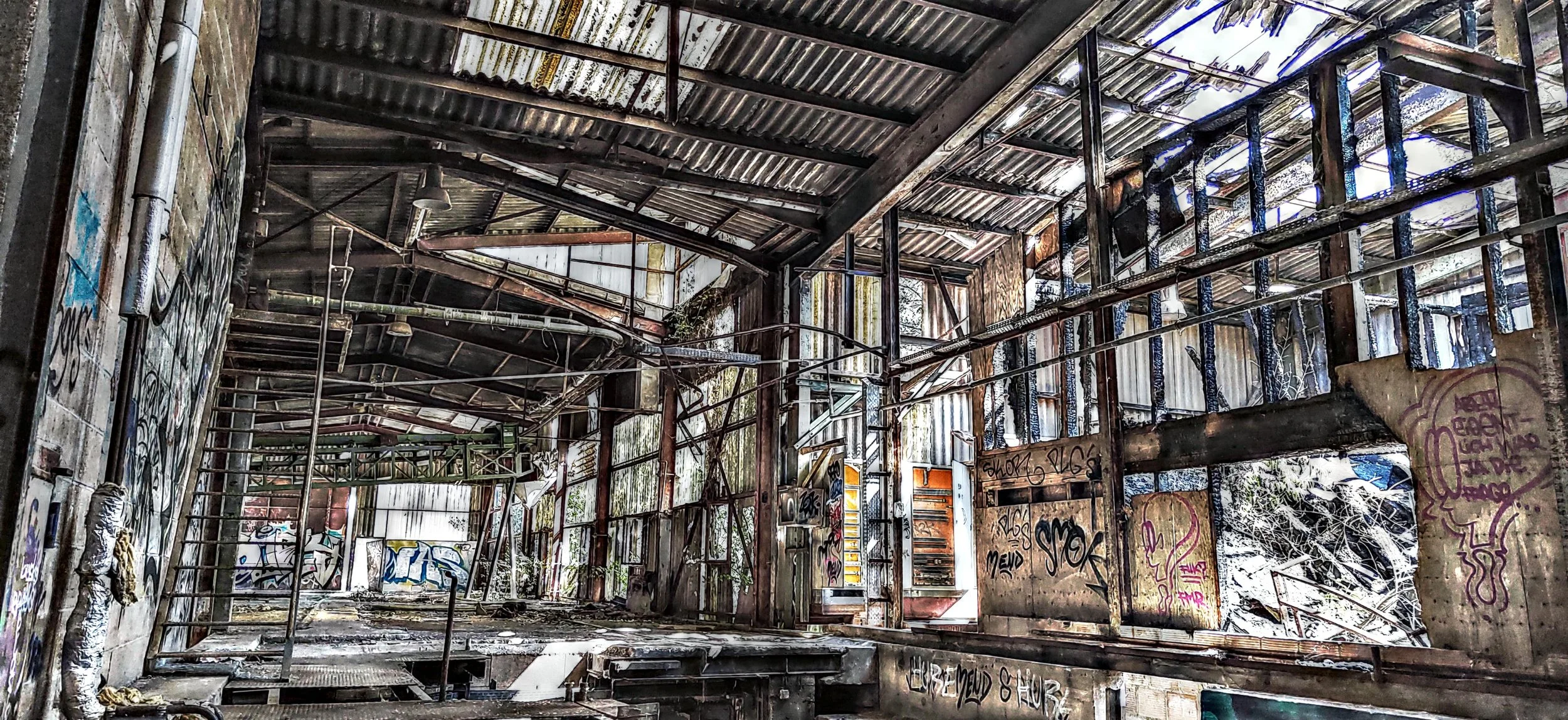 Verfallenes, graffiti-beschmiertes Industriegebäude mit Metallstrukturen und kaputten Wänden.