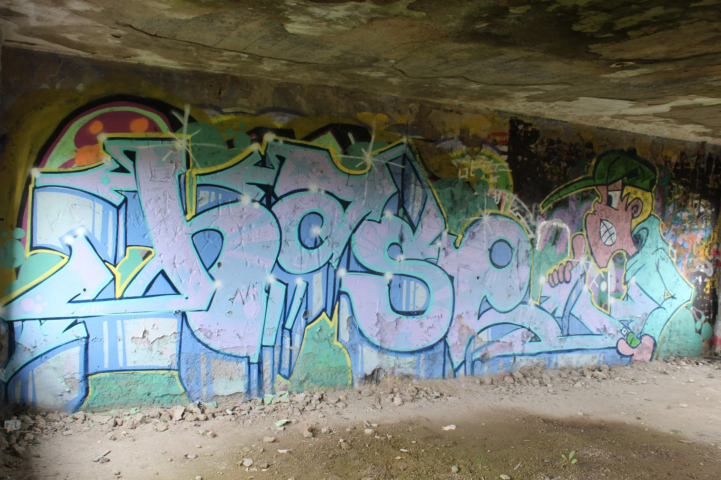 Graffiti an einer Wand in einem Tunnel, das das Wort 'Fokus' zeigt, mit einem cartoonhaften Jungen, der eine grüne Cap trägt und mit einem Stift zeichnet.