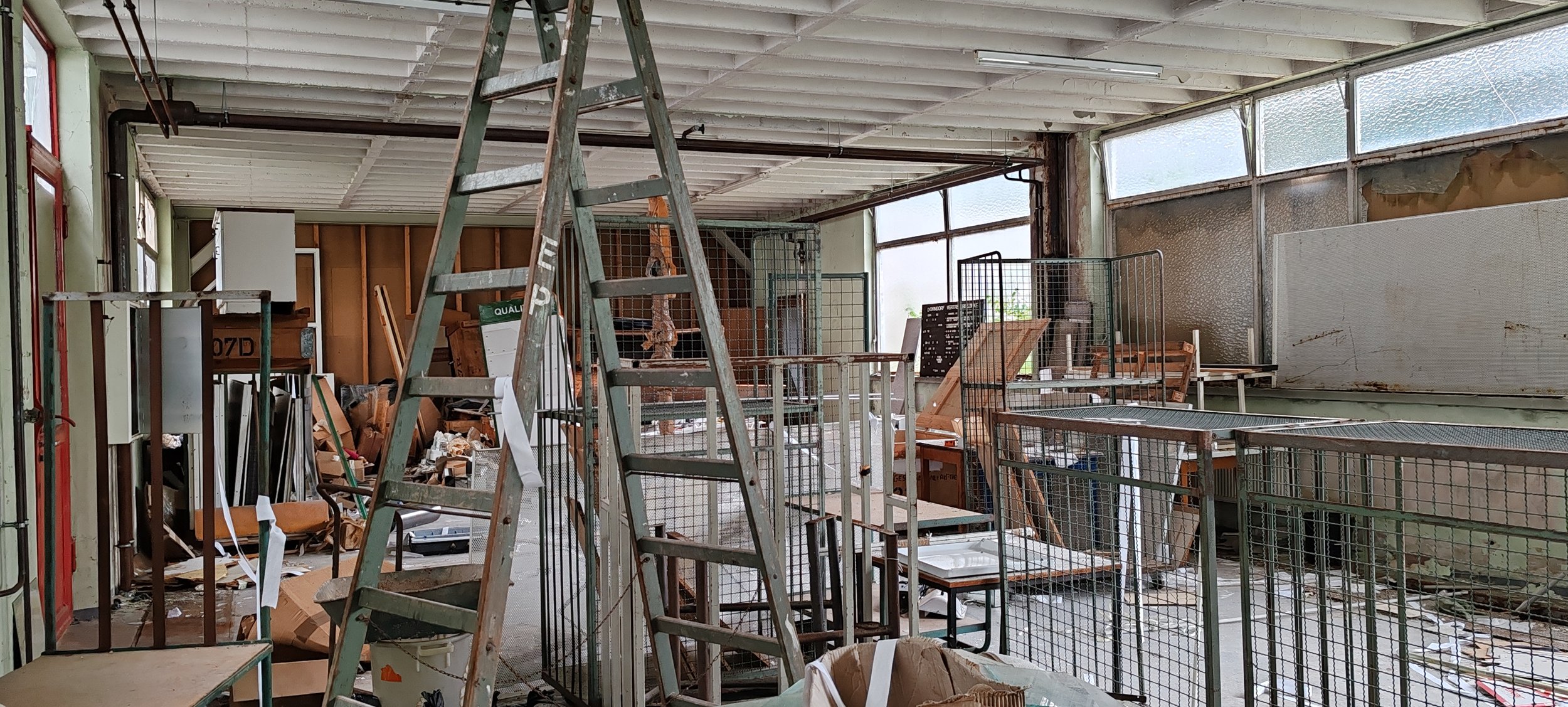 Un unordentlicher Raum mit Werkzeugen, alten Möbeln, einem Leiter und zerbrochenen Fenstern, der stark reparaturbedürftig ist.