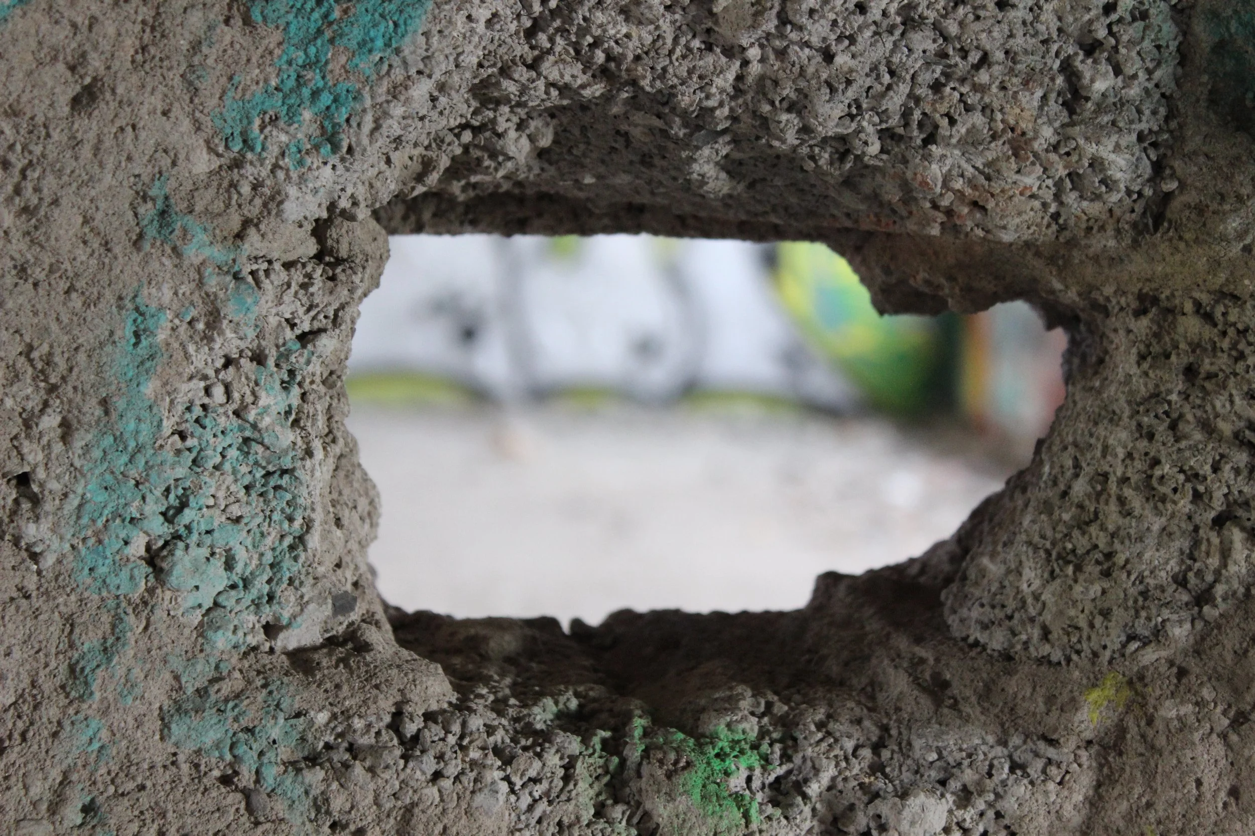 Blick durch ein Loch in einer Betonmauer, die Wand ist grau mit kleinen bunten Sprühfarben und einer rauen Textur.
