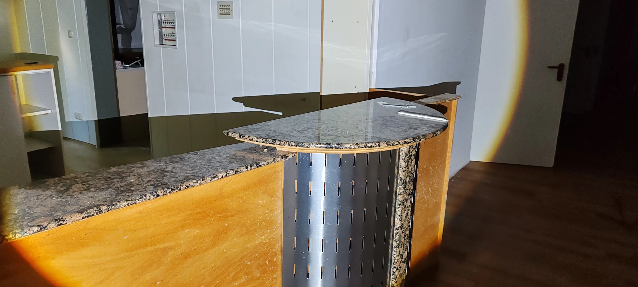 Küche mit einer halbkreisförmigen Theke aus Granit und Holz, einem schwarzen Metallgestell, einem weißen Tür und mehreren Schaltern an der Wand.