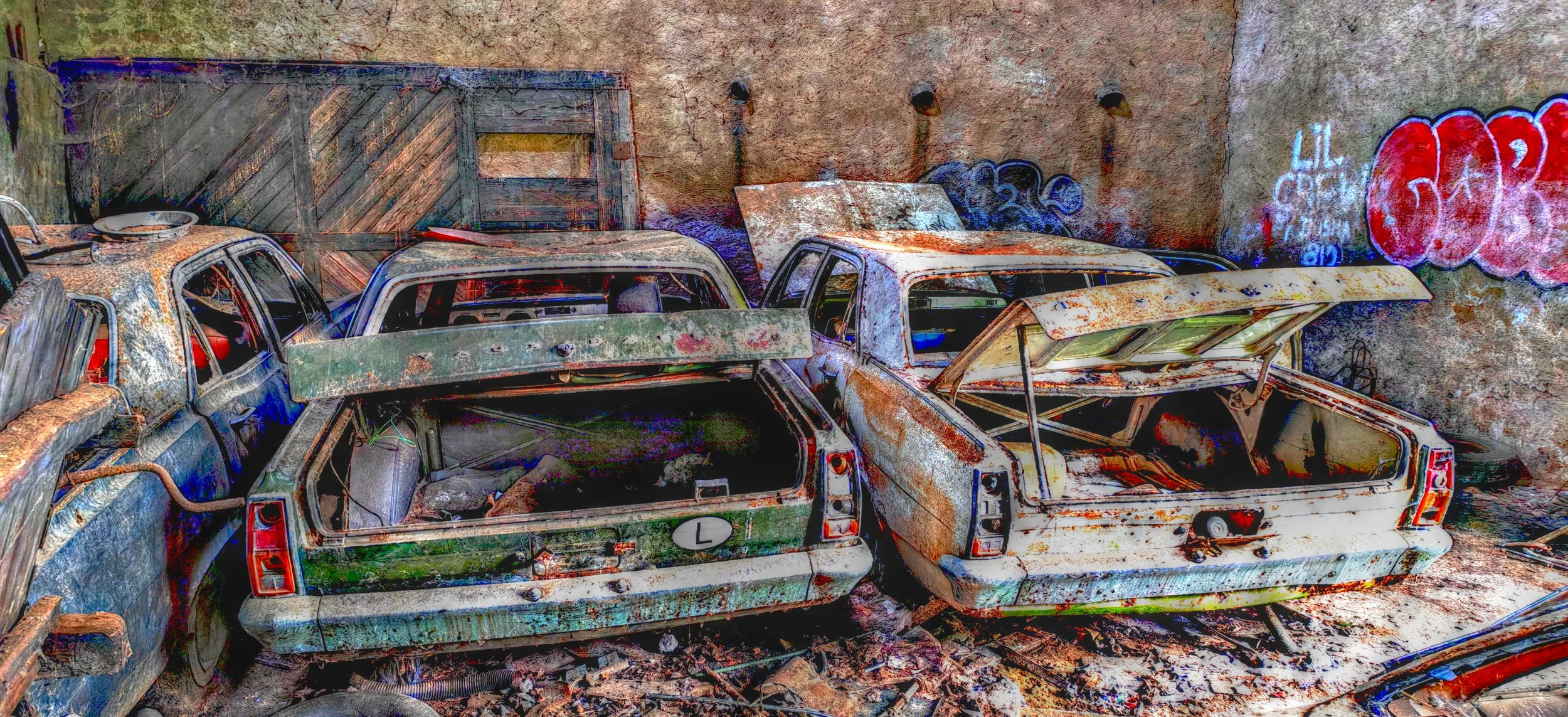 Verlassene, verrostete Autos in einer alten Garage mit Graffiti an der Wand.
