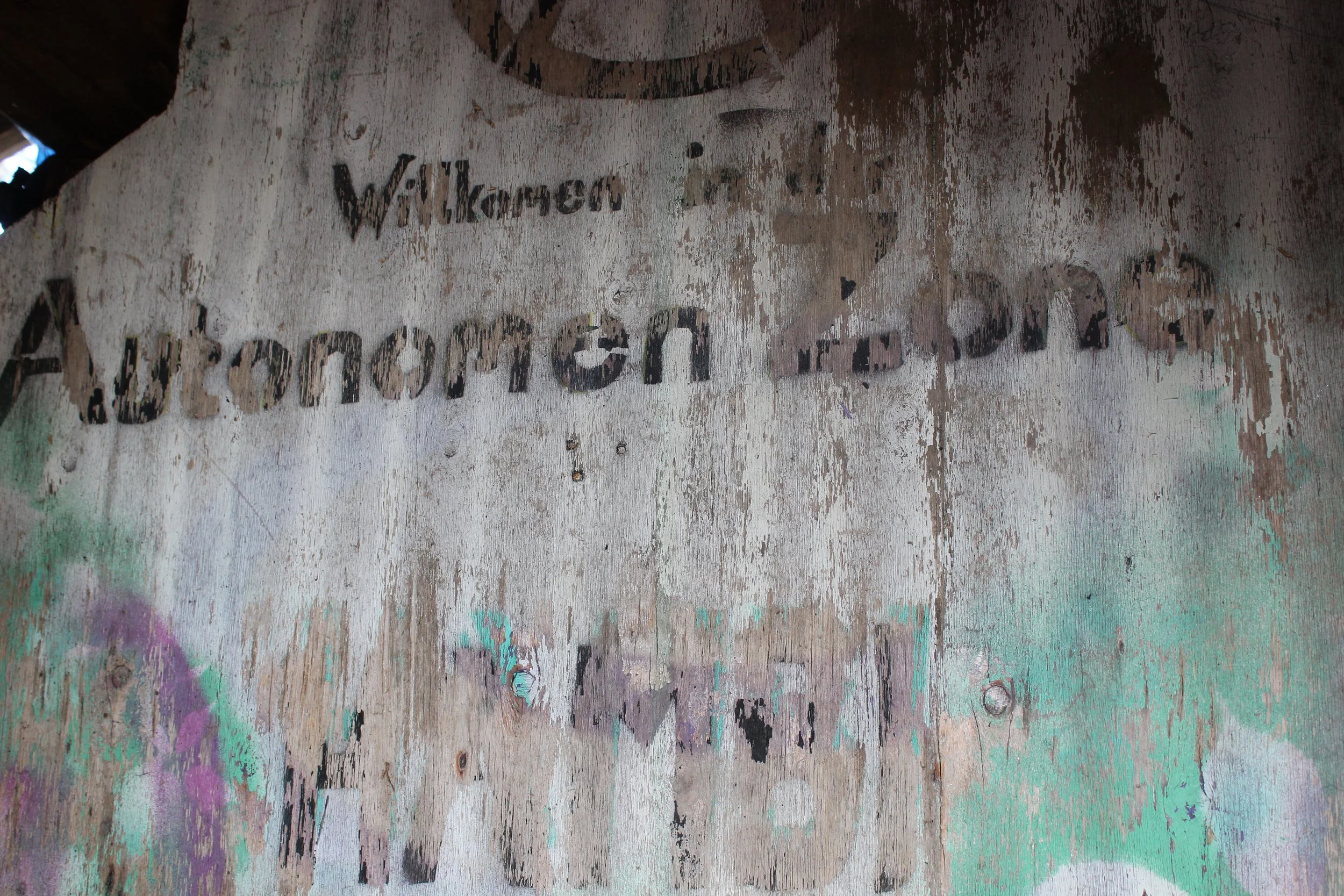 Verwitterte Wand mit verblasster Graffiti- und Schriftkunst, die Begrüßung auf Deutsch zeigt.