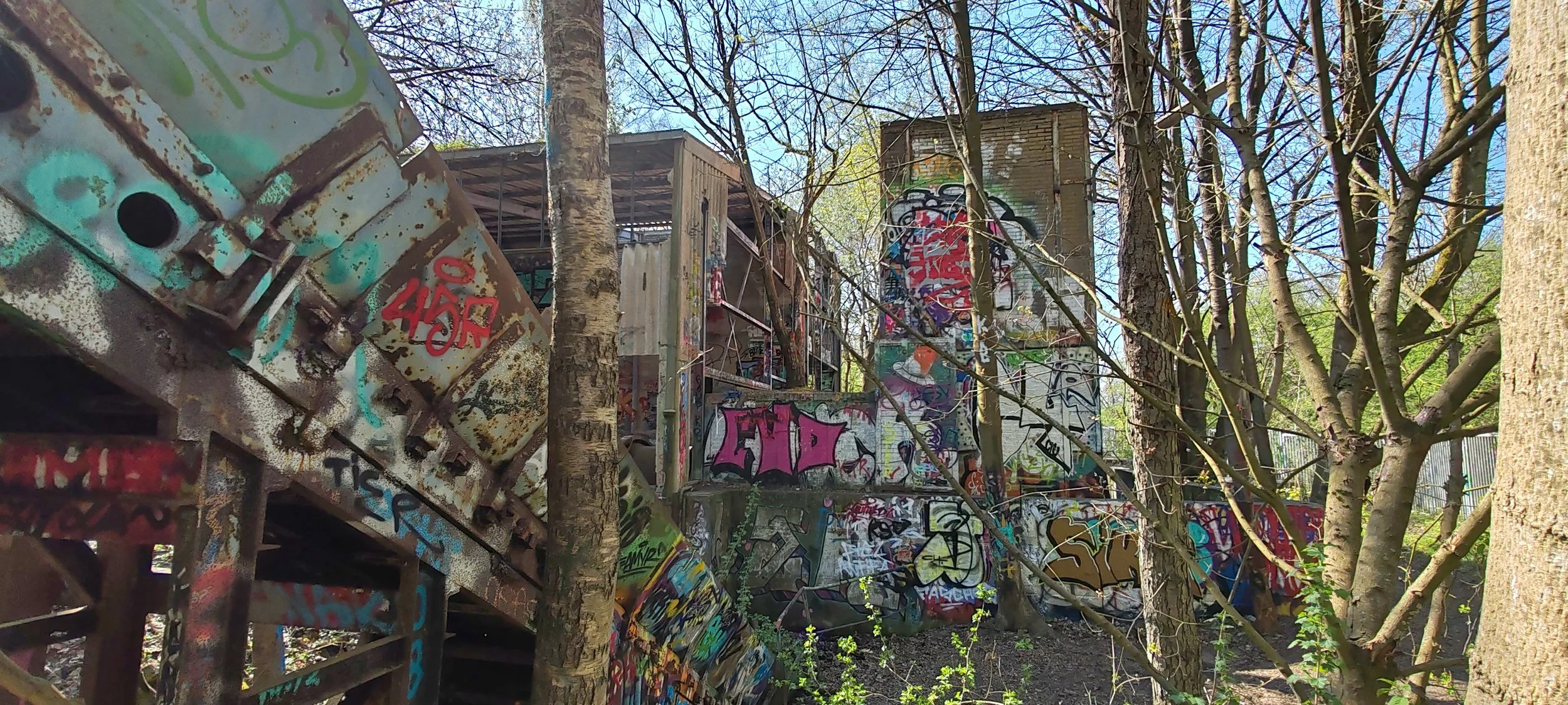 Verfallene, mit Graffiti bedeckte Gebäude und Treppen im Wald, umgeben von Bäumen und Ästen.
