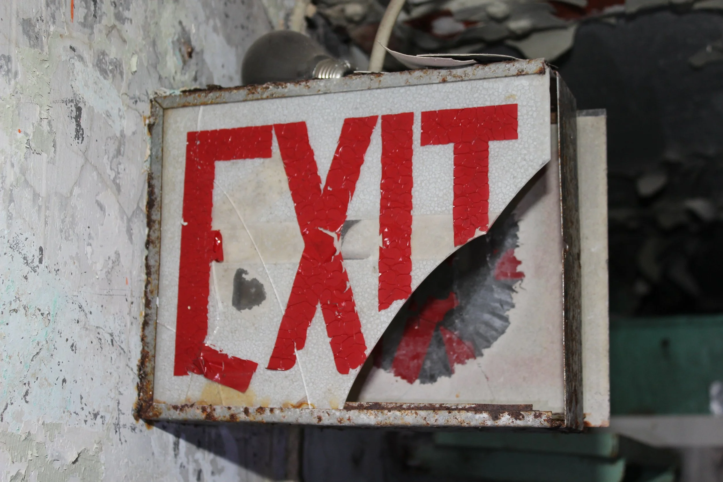 Verrosteter, beschädigter Rauchmelder mit abblätternder Beschilderung und offenem Deckel, auf einer zerkratzten Oberfläche.