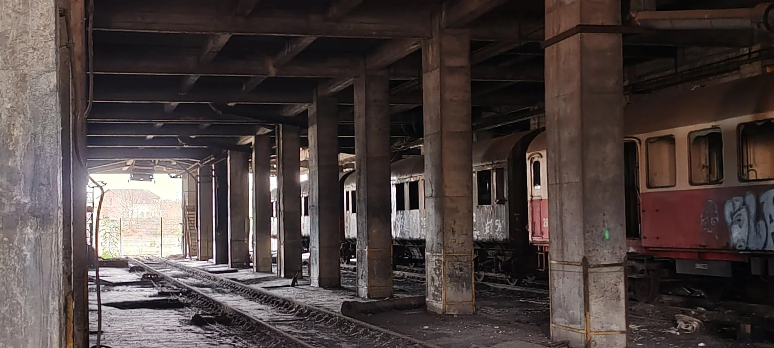 Verlatenes Bahnhofsgebäude mit verrosteten Zügen und schmutzigen Gleisen.