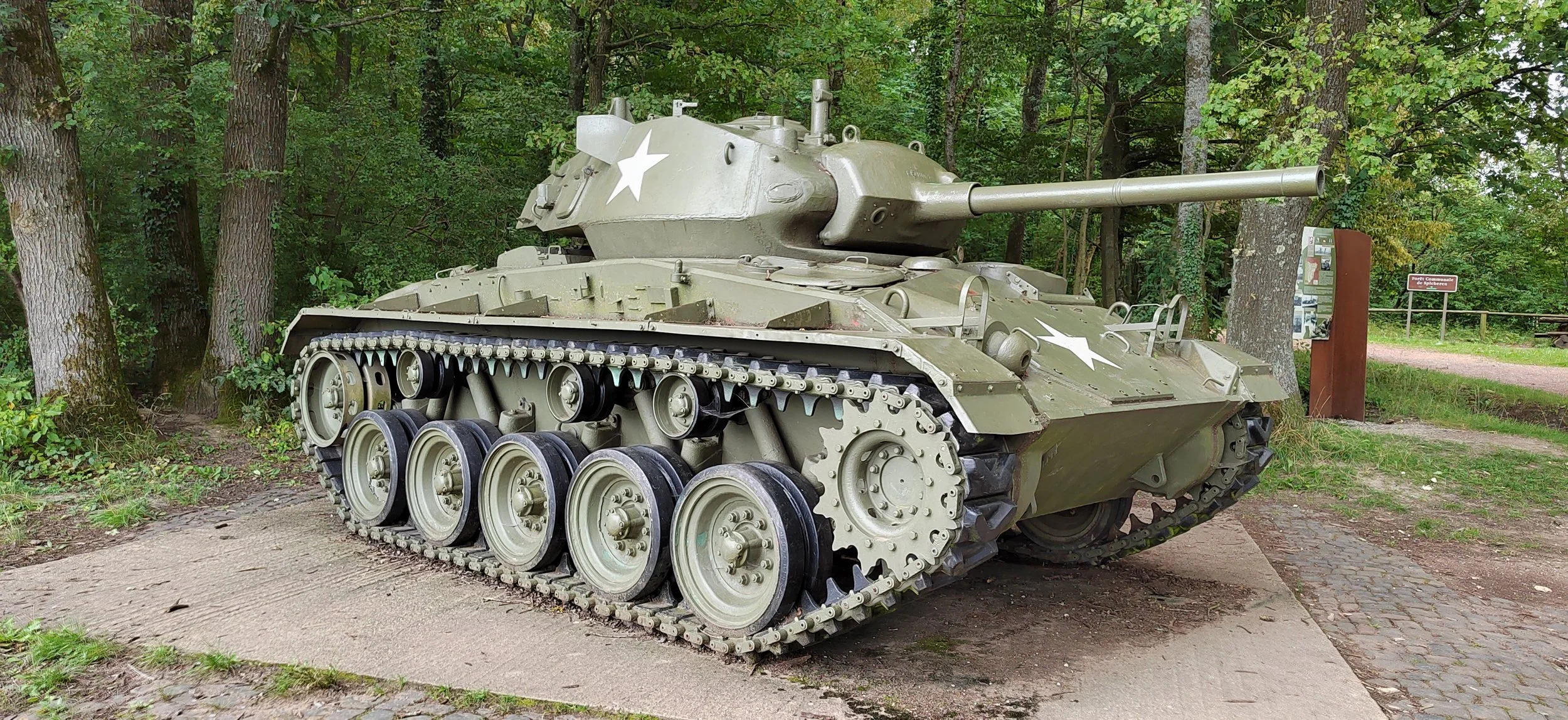 Ein Militär-Panzer mit grüner Tarnung und weißen Sternen vor einem Wald im Freilichtmuseum.