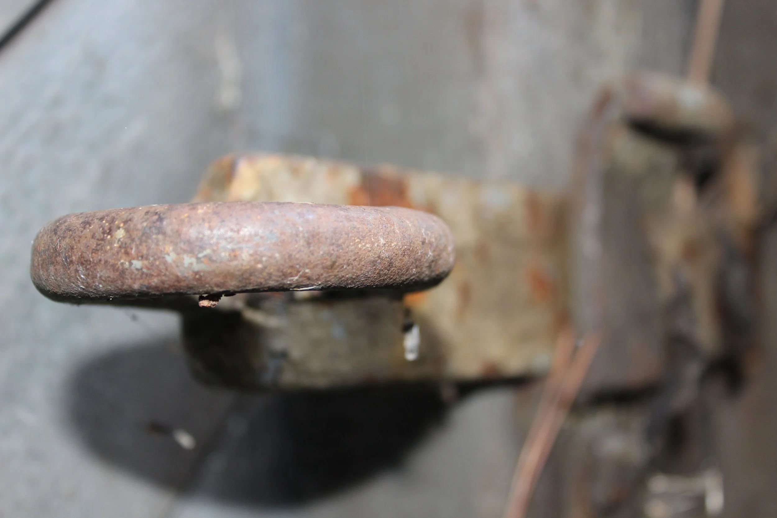 Nahaufnahme eines alten, rostigen Metallrings auf einer Metallplatte, mit weiteren metallischen Gegenständen im Hintergrund.