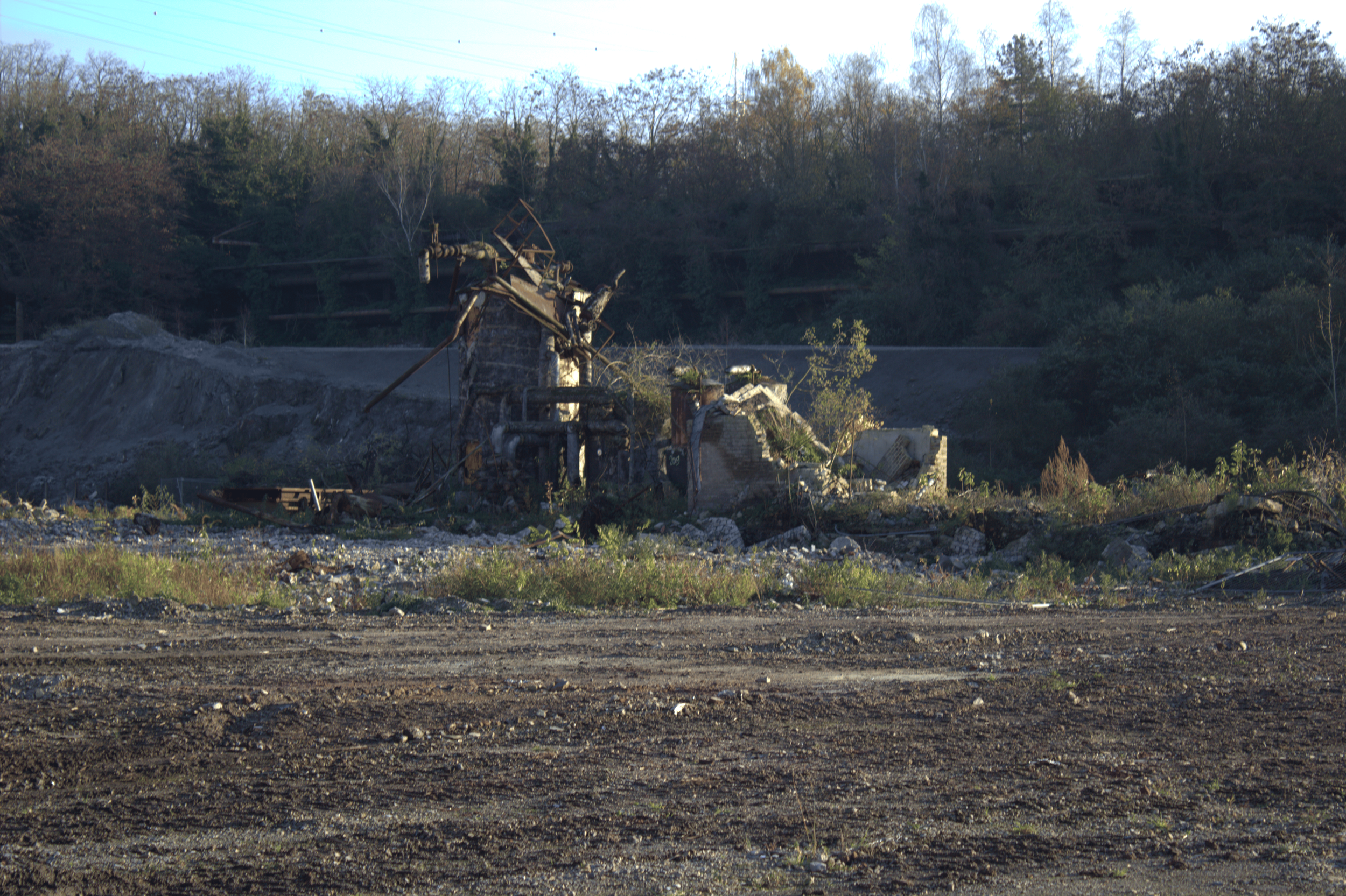 Zerstörte Fabrikruine in einer ländlichen Gegend, umgeben von Bäumen und unbefestigtem Boden.