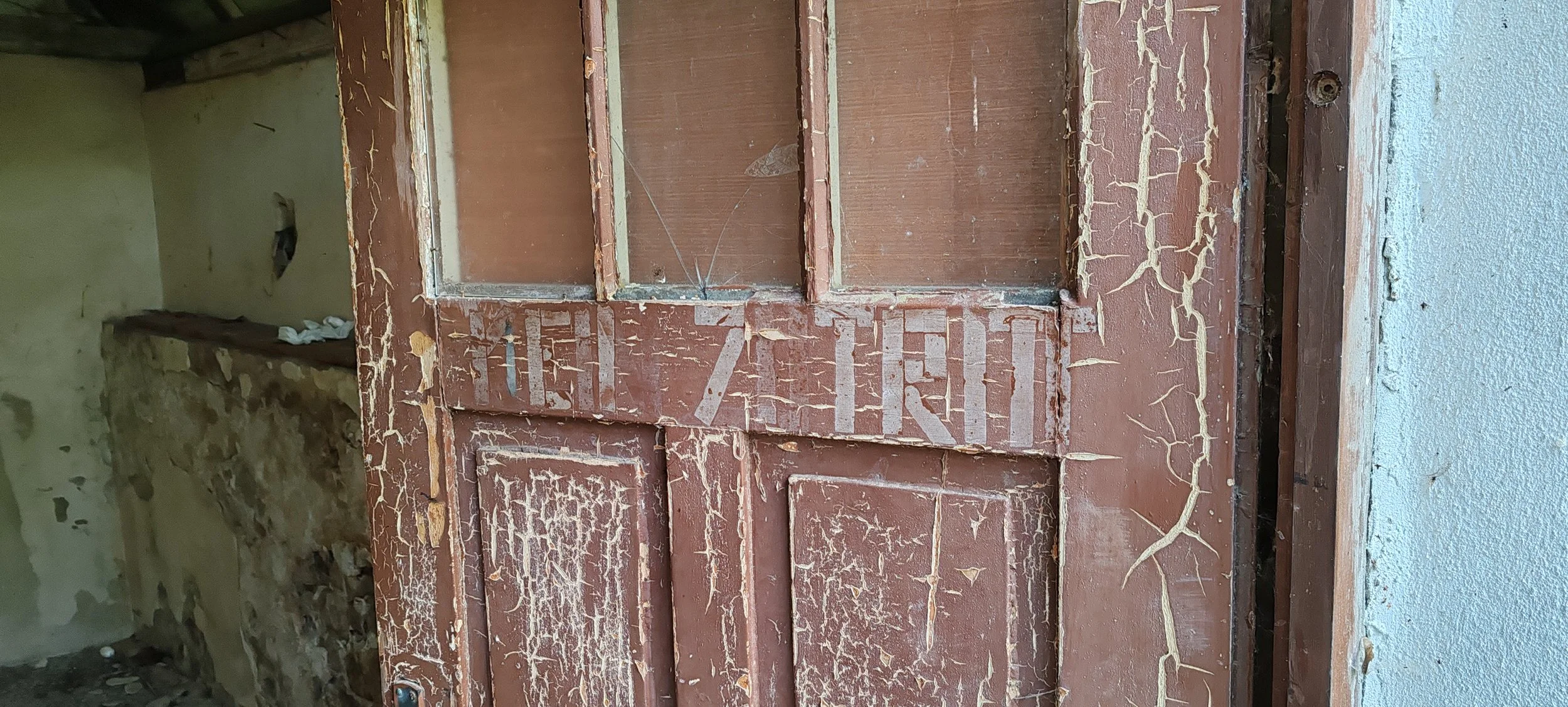 Alter Holz- oder Türrahmen mit verblasster roter Farbe und sichtbaren Rissen, im Hintergrund eine beschädigte Wand mit Putz und einem kleinen Loch.