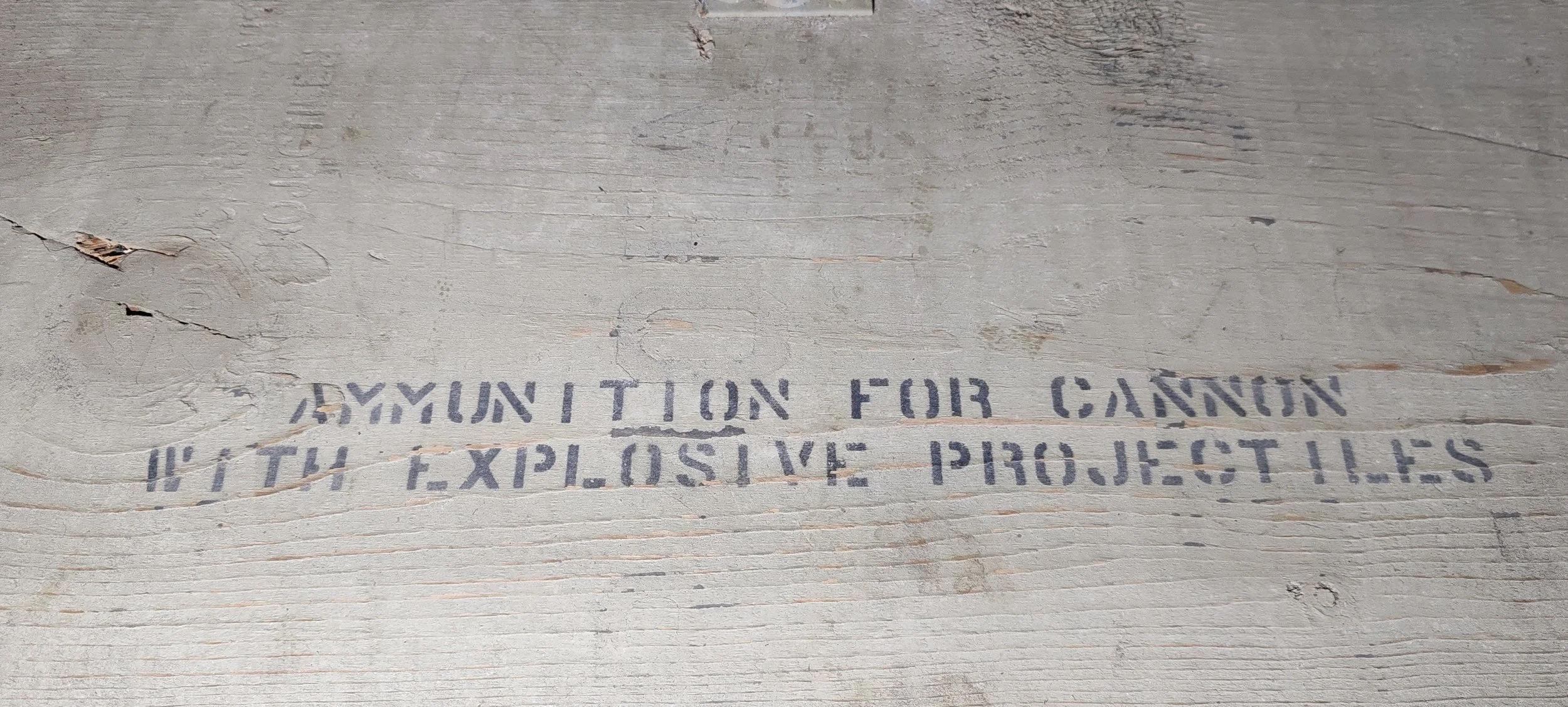 Verblasste, stark verzerrte Aufschrift auf einer Holzoberfläche mit Kratzern und Rissen, die vermutlich eine Warnung für den Umgang mit explosiven Materialien ist.