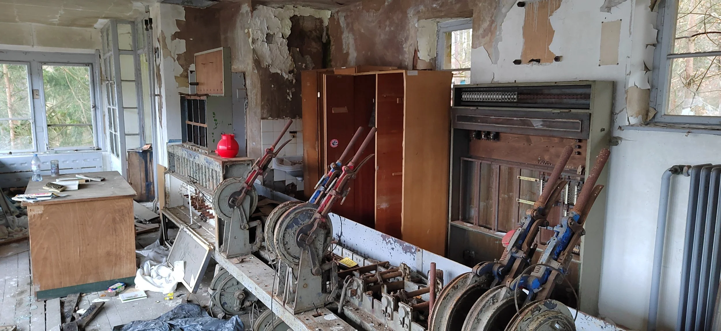 Ein verlassener, renovierungsbedürftiger Raum mit alten Möbeln, einem handbetriebenen Musikinstrument und zerbrochenen Fenstern. Der Raum ist chaotisch mit Staub und Müll.