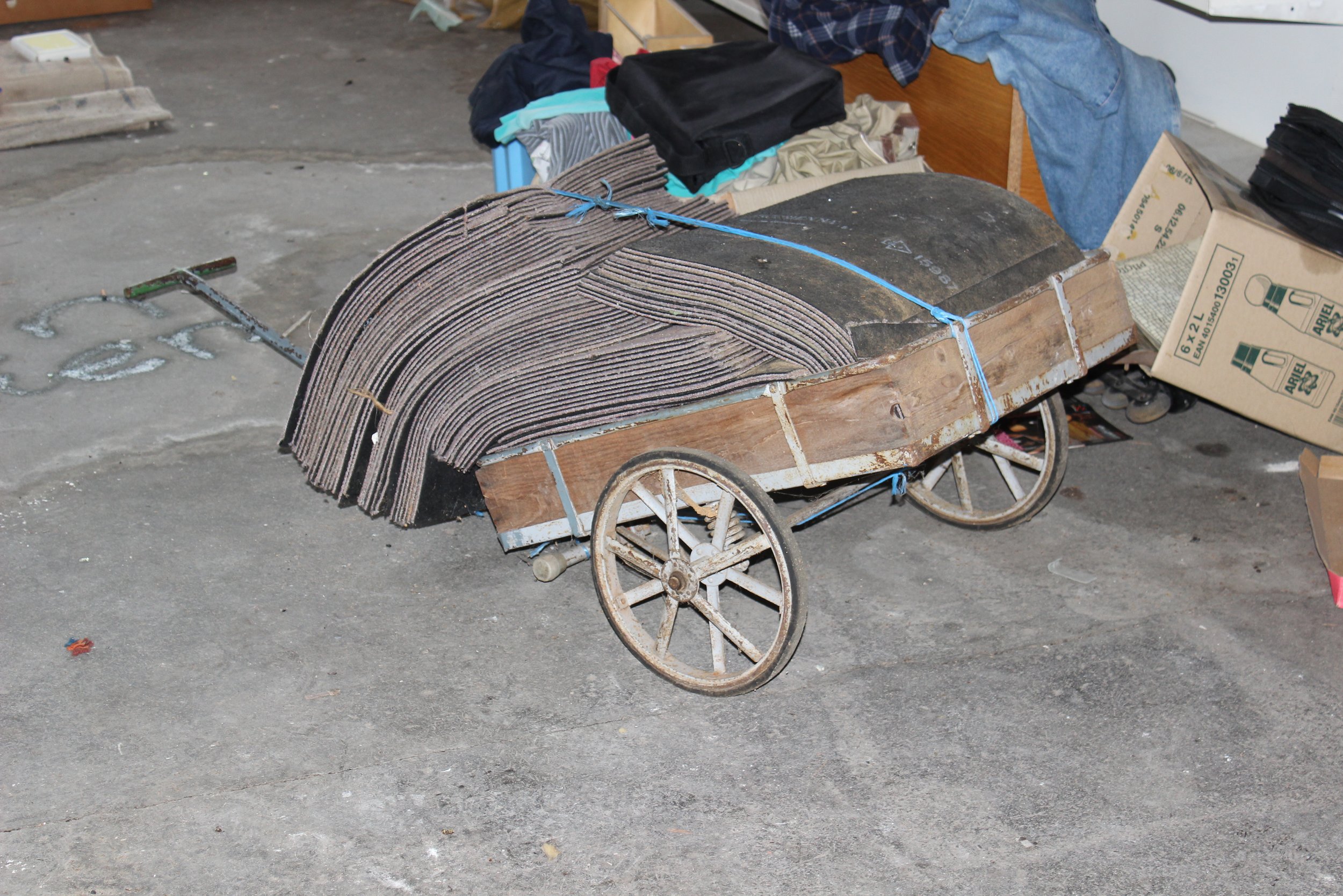 Ein alter Handwagen mit Holzrahmen und Metallrädern, beladen mit schwarzen und braunen Teppichen.