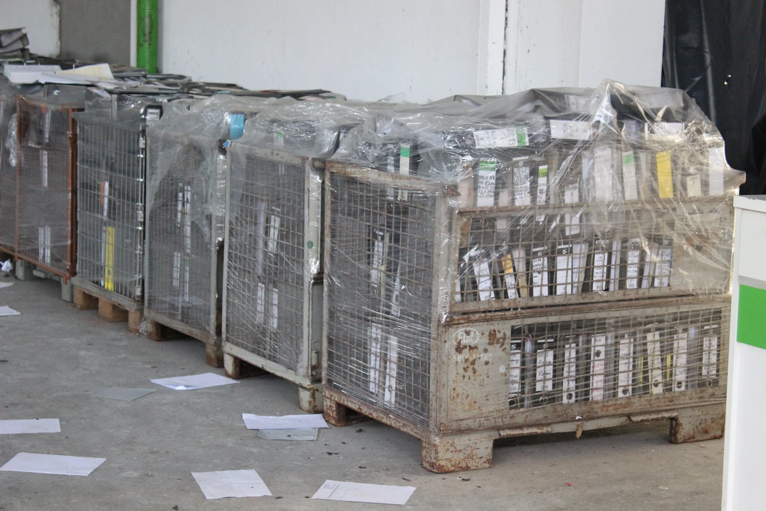 Altreifenkäfige mit Papierstücken verstreut auf dem Boden in einer Lagerhalle.