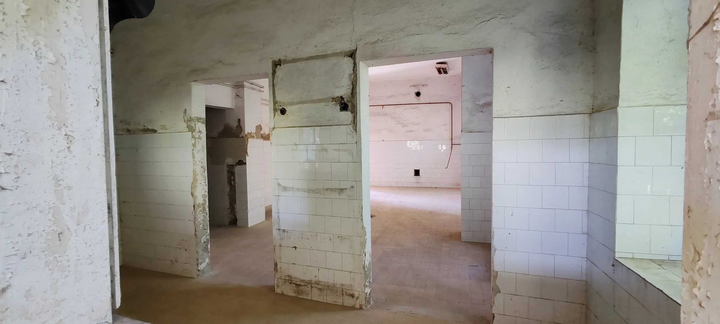 Ein verlassener, ungewohnter Raum mit weißen, teilweise beschädigten Fliesen an den Wänden, offensichtlich im Umbau oder Verfall.