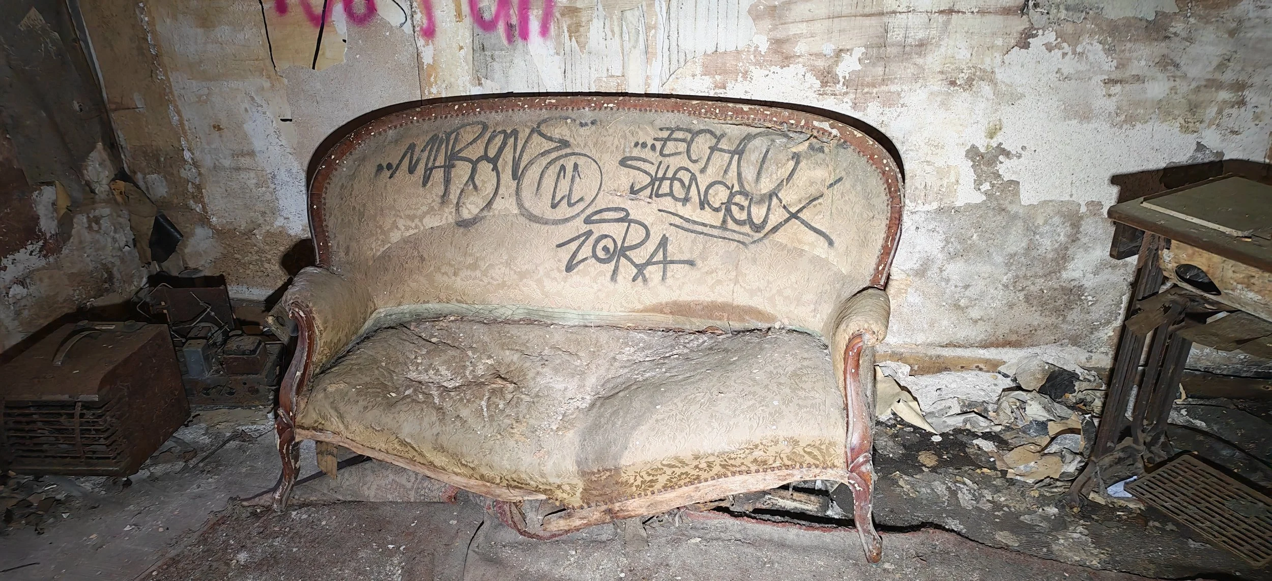 Verfallene, alte Couch in einem verfallenen Raum mit Graffiti an der Wand.