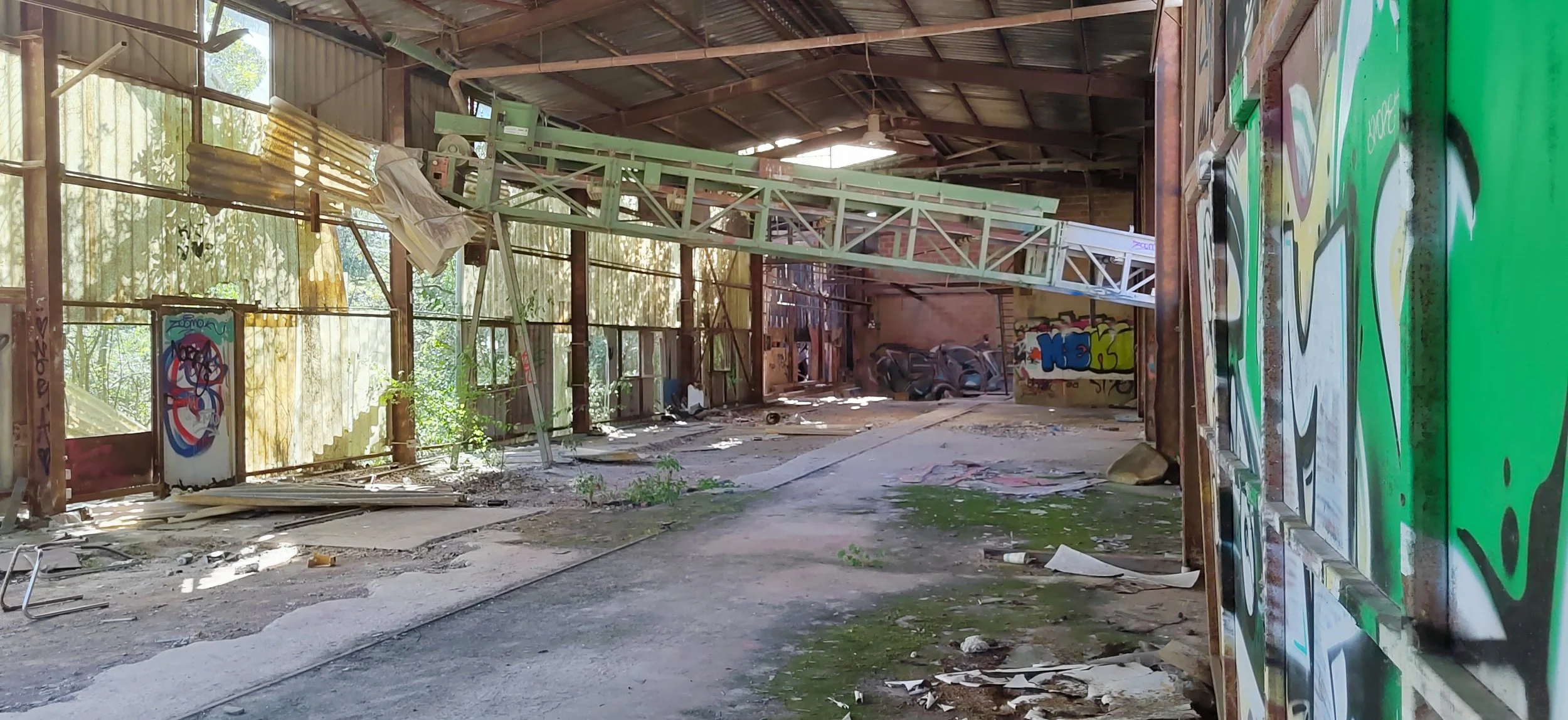 Verlassener, verfallener Gebäudekomplex mit Graffiti an den Wänden, zerbrochenen Fenstern und viel Schmutz auf dem Boden, mit einem großen LKW-Hubwagen im Inneren.