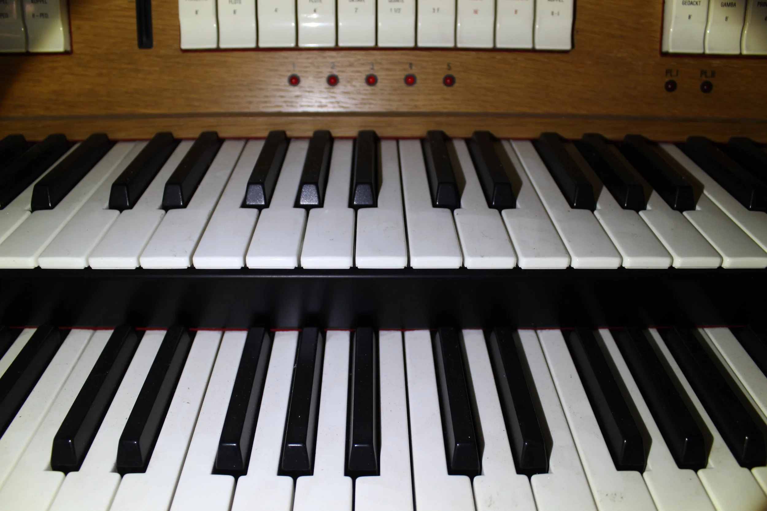 Nahaufnahme von zwei Klaviertastaturen, die übereinander angeordnet sind, mit schwarzen und weißen Tasten und einem Holzrahmen.