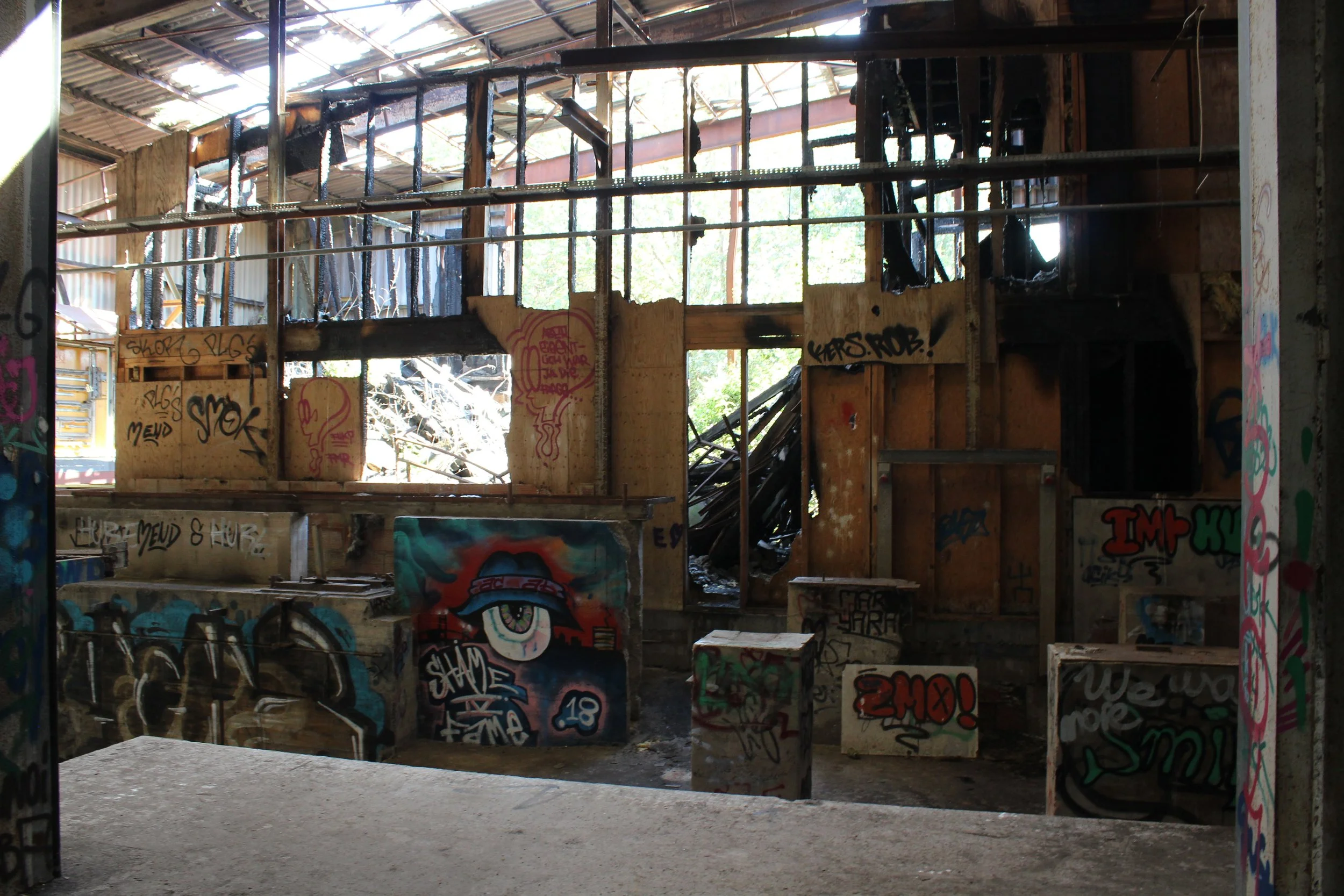 Verlassene, graffiti-verschmierte Innenraumstruktur mit Holzwänden, abgedecktem Dach und zerstörten Fenstern.