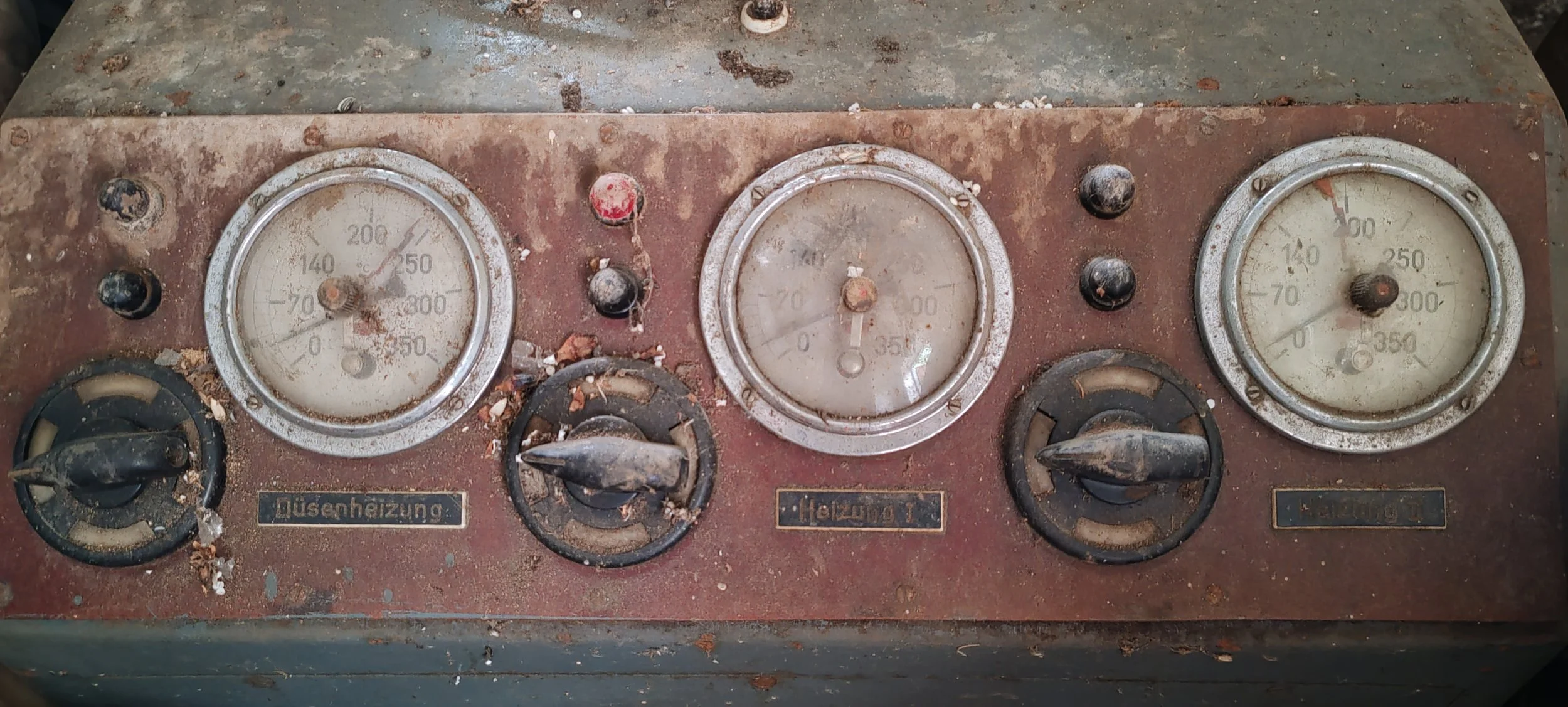 Alteres, verrostetes Steuerpult mit drei Uhren und vier Drehknöpfen, Beschriftung in Deutsch, schmutzig und staubig.